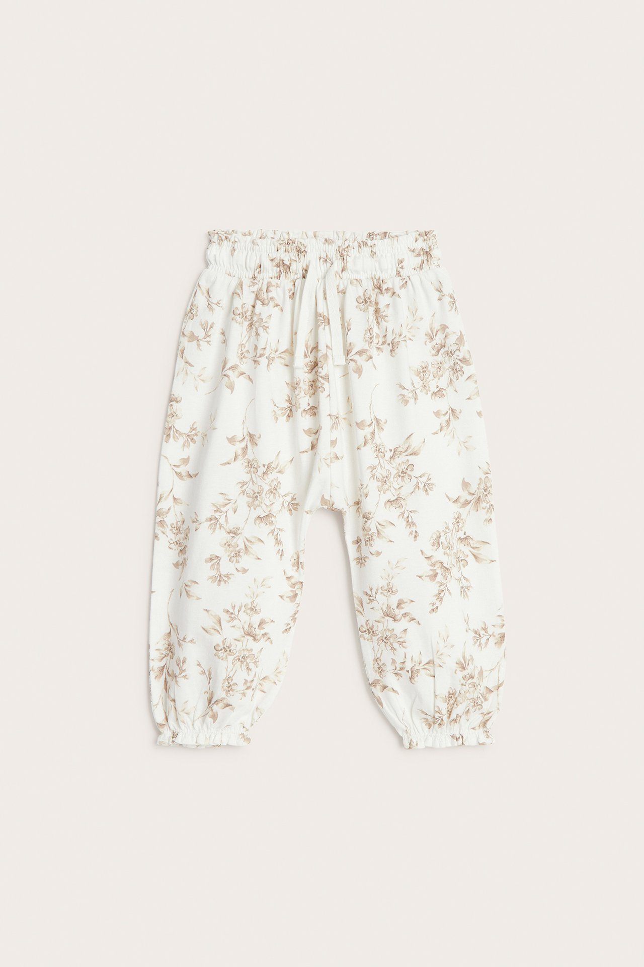 Framifrån: Off-white baby jerseybyxor med brunt blommigt mönster, vida ben, resår i midjan och muddar.