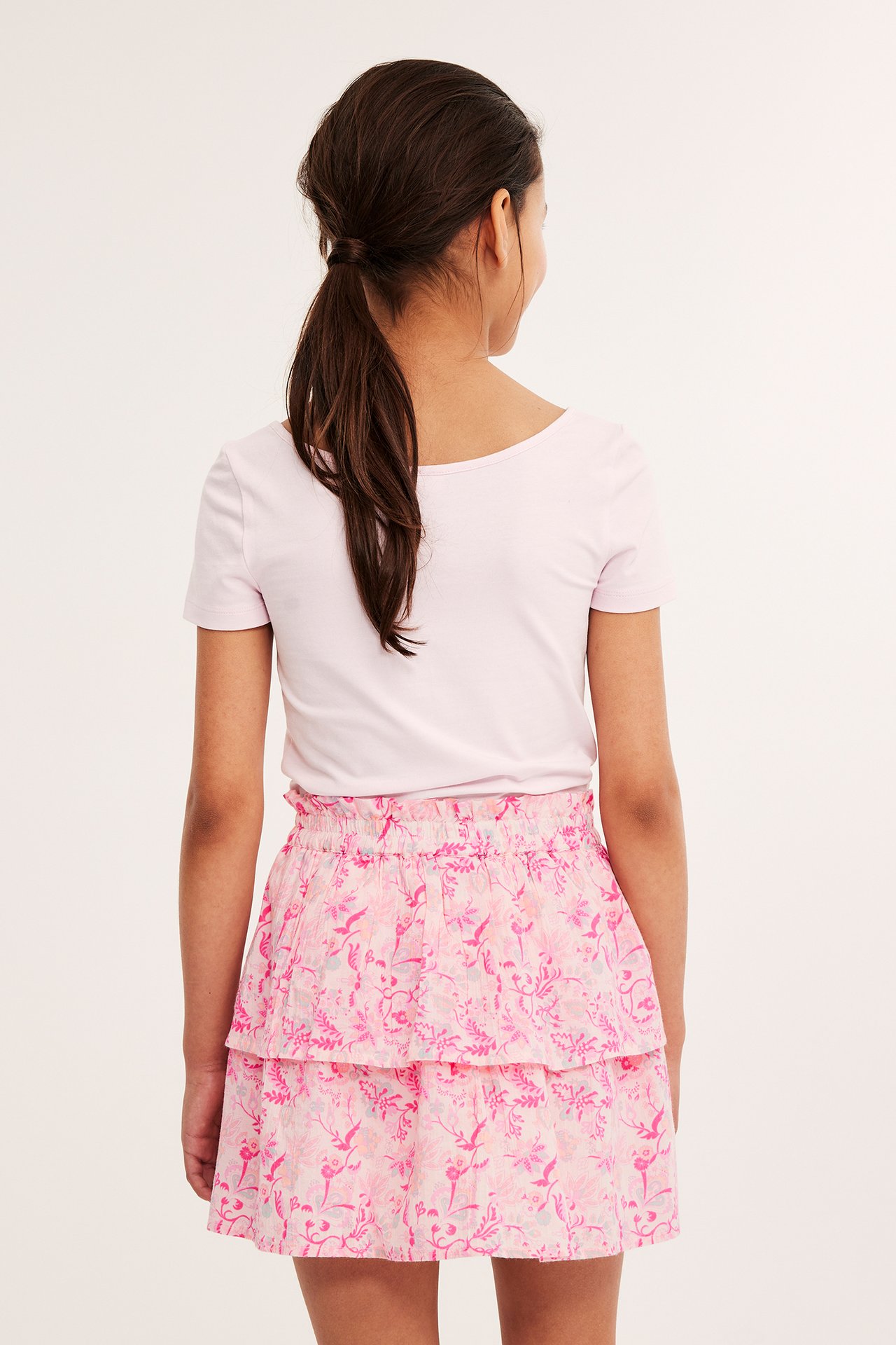 Bakifrån: ett barn i kort rosa mönstrad volangkjol och en ljusrosa t-shirt.