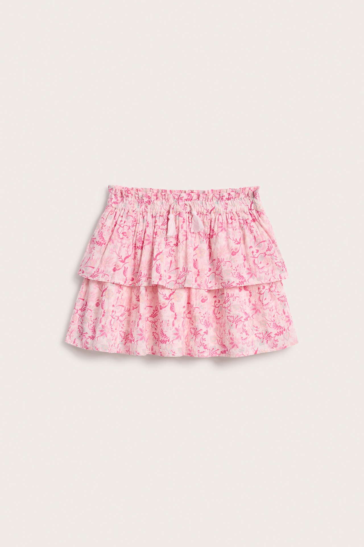 Framifrån: kort rosa mönstrad volangkjol för barn med resår i midjan och tofsar.