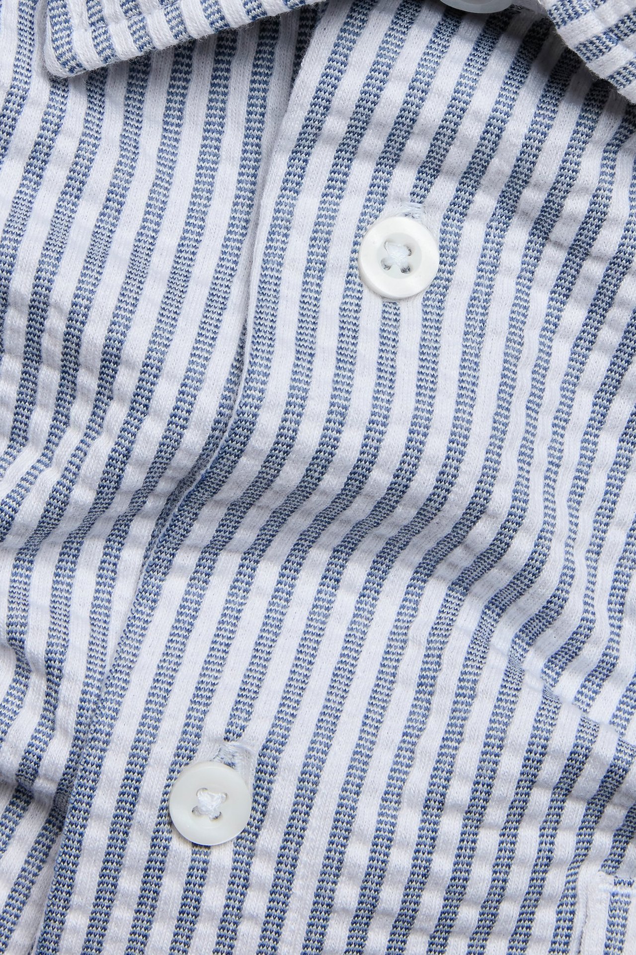 Zbliżenie na granatowo-białą koszulę z krótkim rękawem w paski, z białymi guzikami.