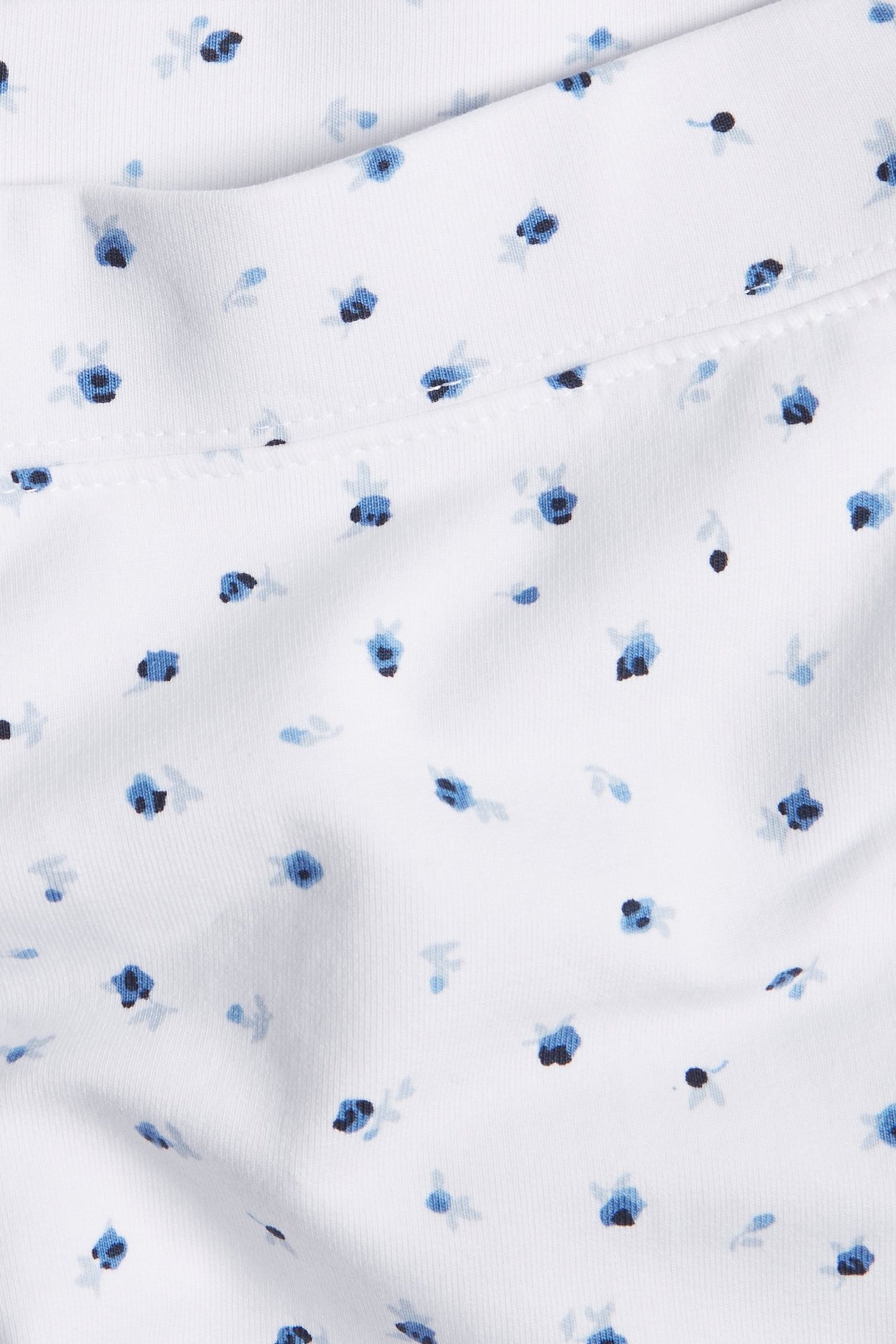 Zbliżenie białych wzorzystych krótkich spodenek rowerowych z niebieskim kwiatowym wzorem i widocznym szwem.