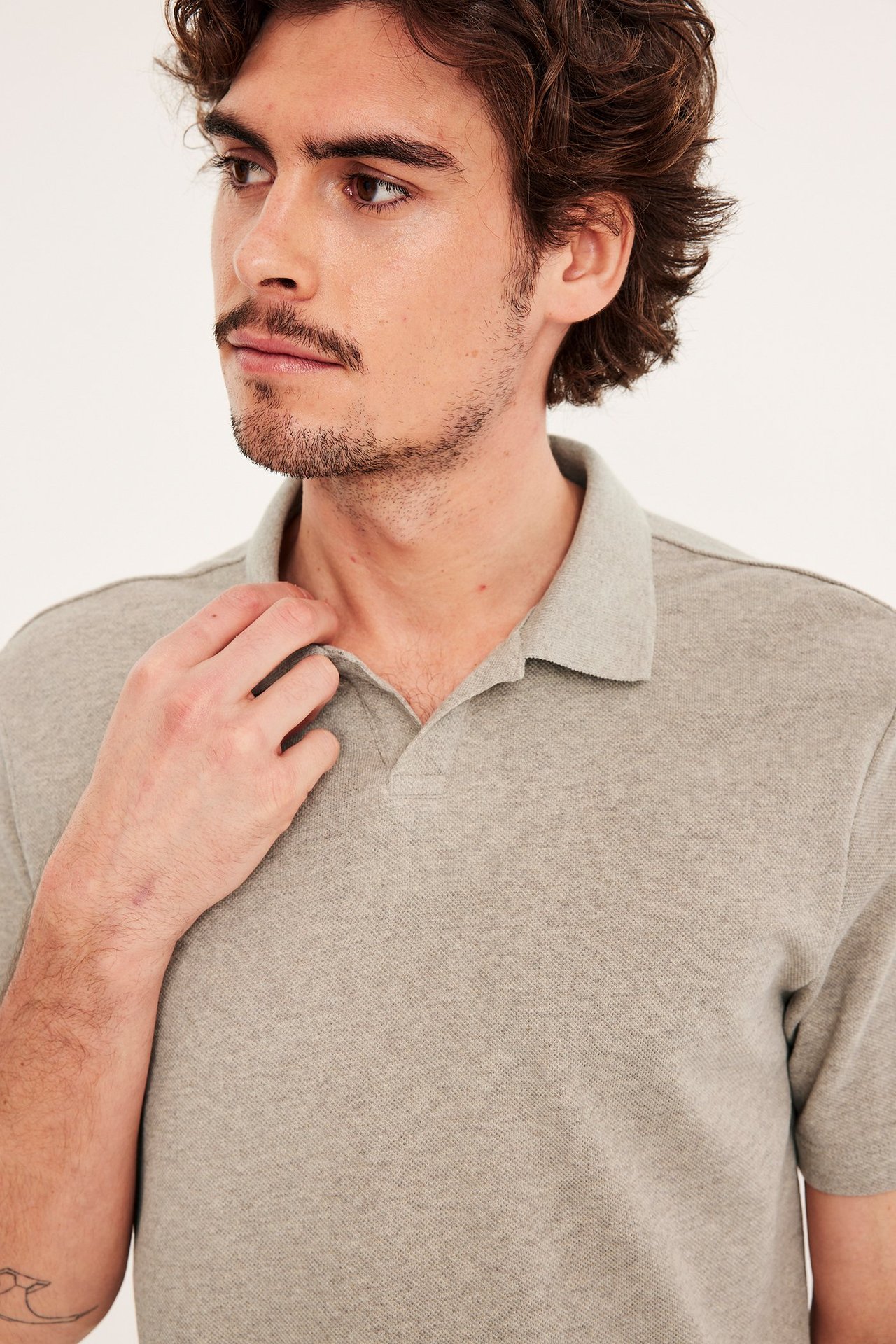 Lähikuva edestä miehestä, jolla on beigenvärinen meleerattu pikeepaita, käsi kauluksella.