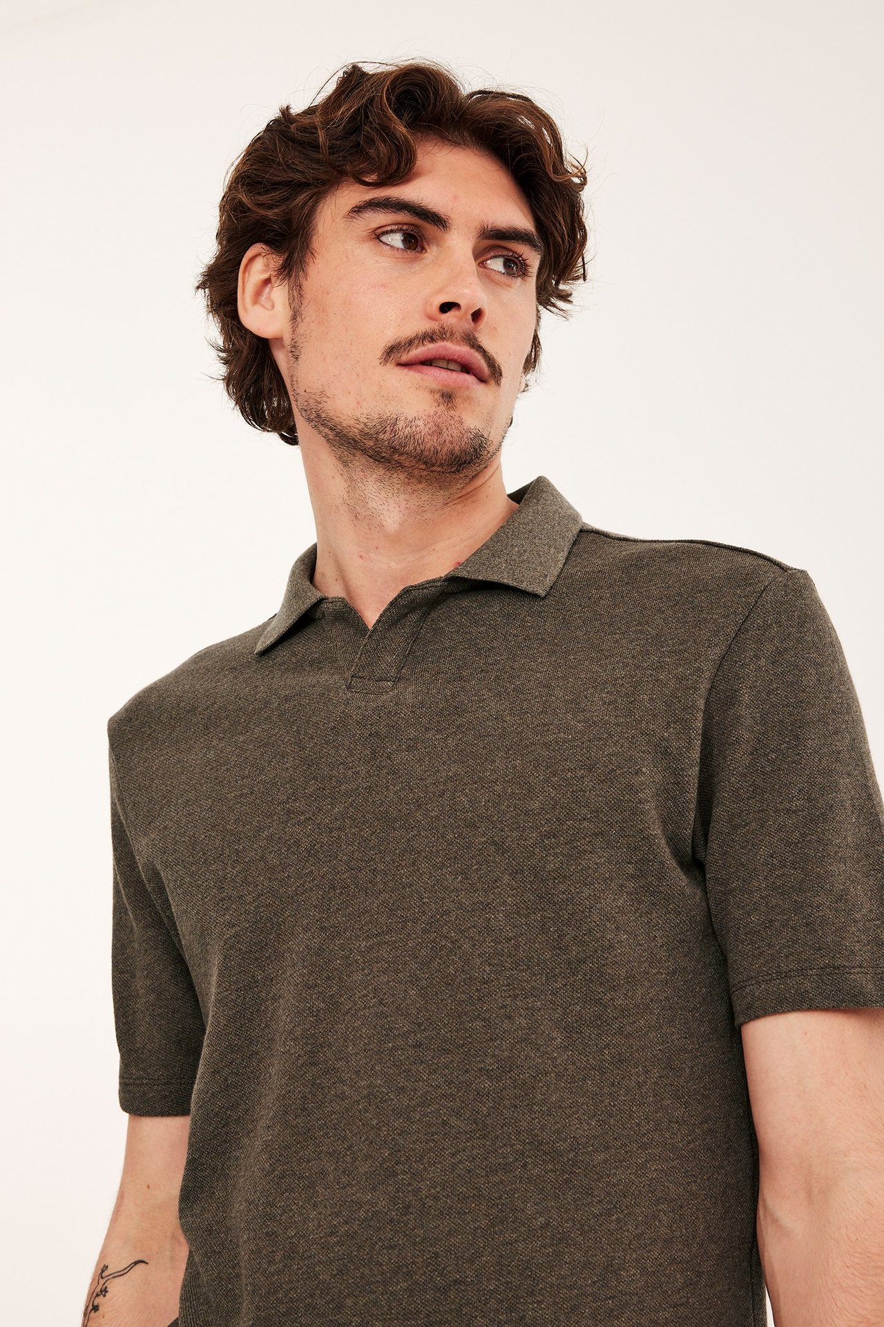 Lähikuva edestä miehestä, jolla on ruskeanmelange puuvillapikeepaita V-pääntiellä.