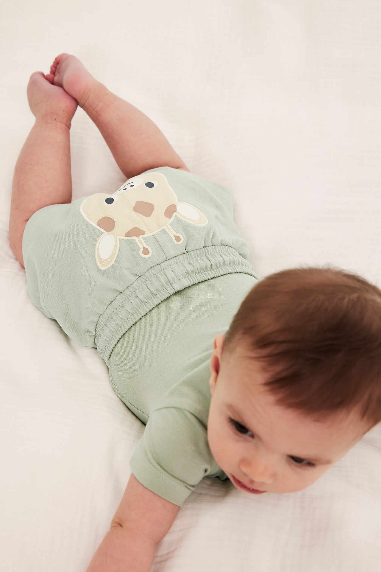 Høyt vinkelbilde av en baby i grønne bomullsshorts med sjiraffapplikasjon og matchende grønn body.