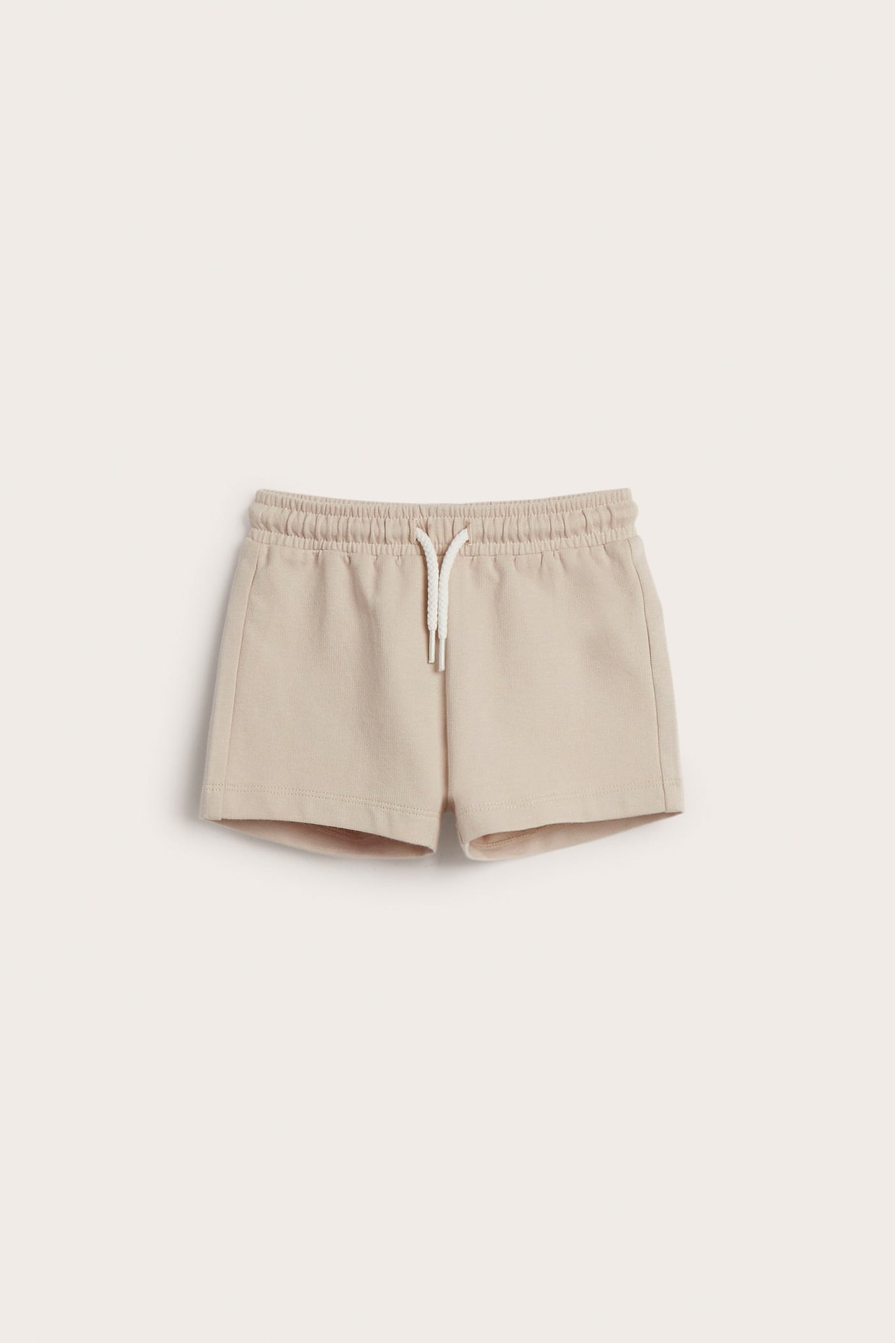 Frontvisning av beige baby-bomullsshorts med elastisk midje og hvit snøring.