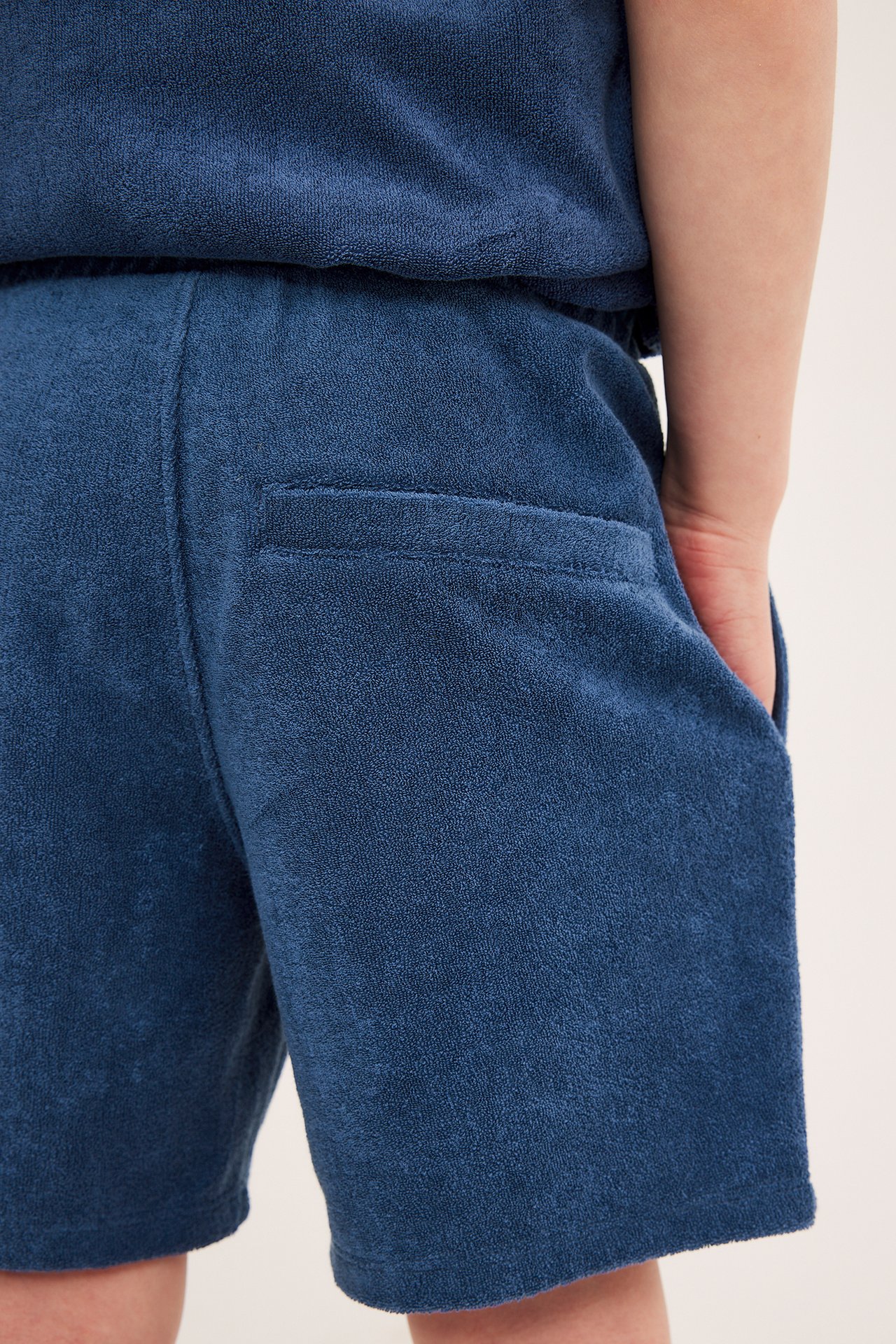 Nærbilde av et barn i mørkeblå frottéshorts med lommer og matchende topp.