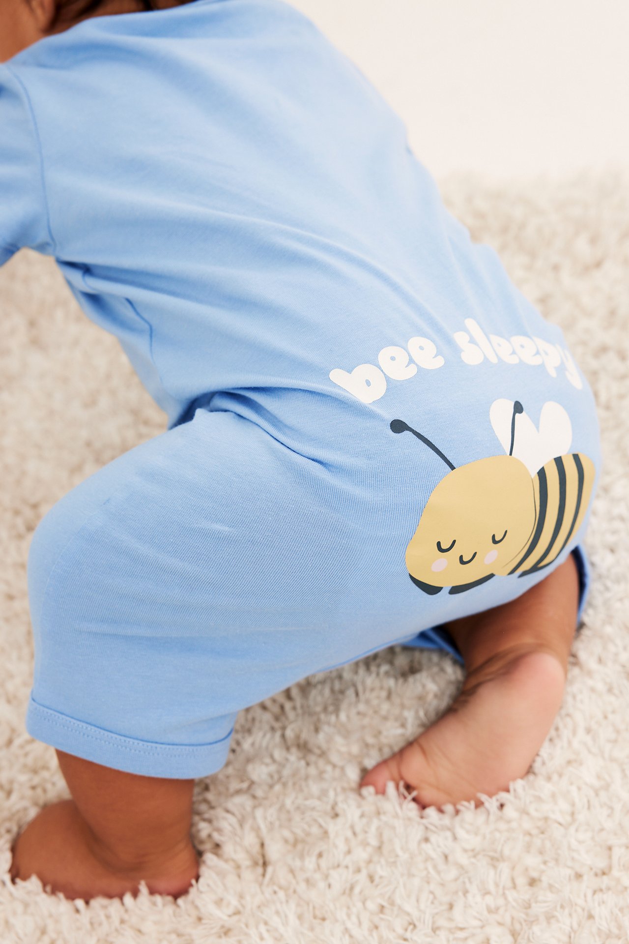 Widok z tyłu na dziecko w jasnoniebieskiej, krótkiej piżamie bawełnianej z napisem 'bee sleepy' i pszczółką.