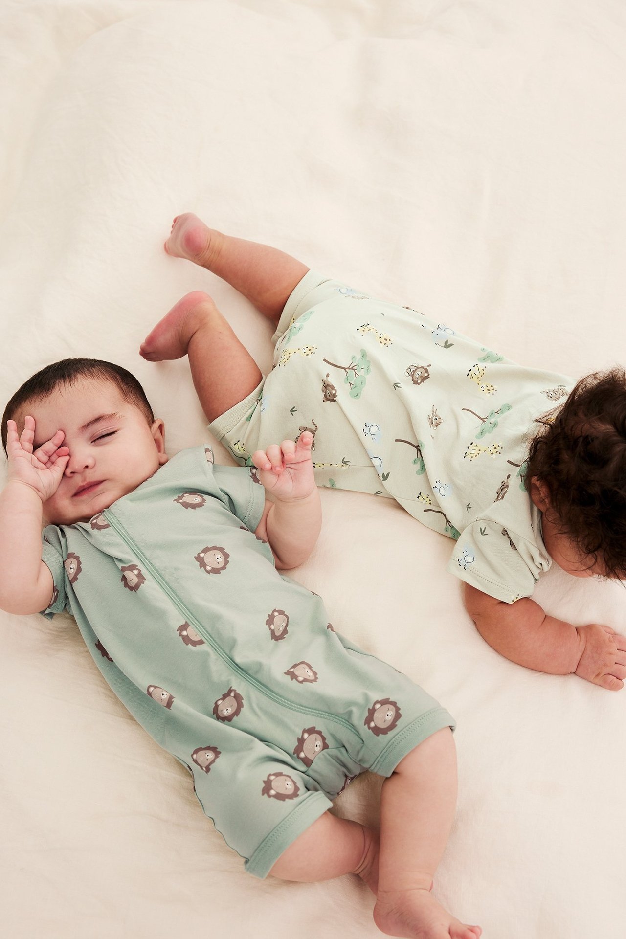 Dwa niemowlęta w krótkich pajacykach: jeden zielony z nadrukiem lwa, drugi jasnozielony z nadrukiem dżungli.