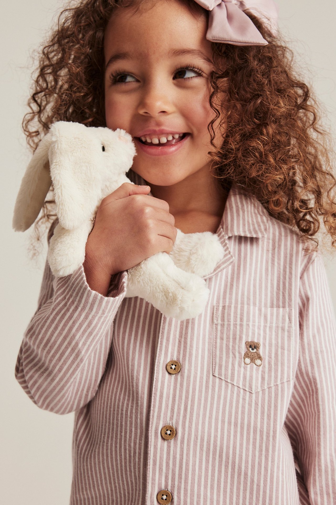 Nærbilde av et barn i rosa stripete pysjamasskjorte med brodert bjørn, holder en hvit kanin.