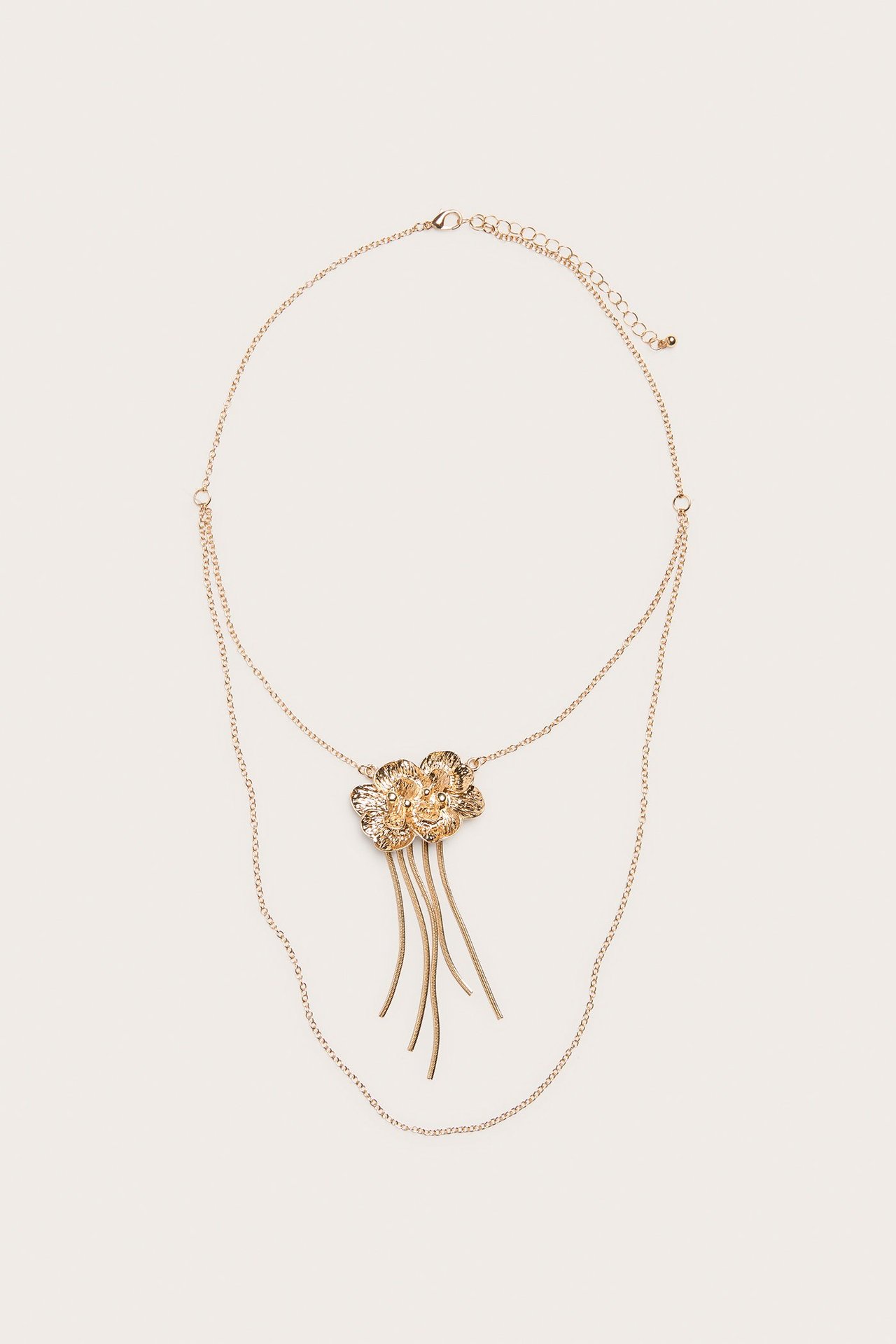 Framsida av ett guldfärgat lagerhalsband med blomhänge och dinglande metalltrådar.