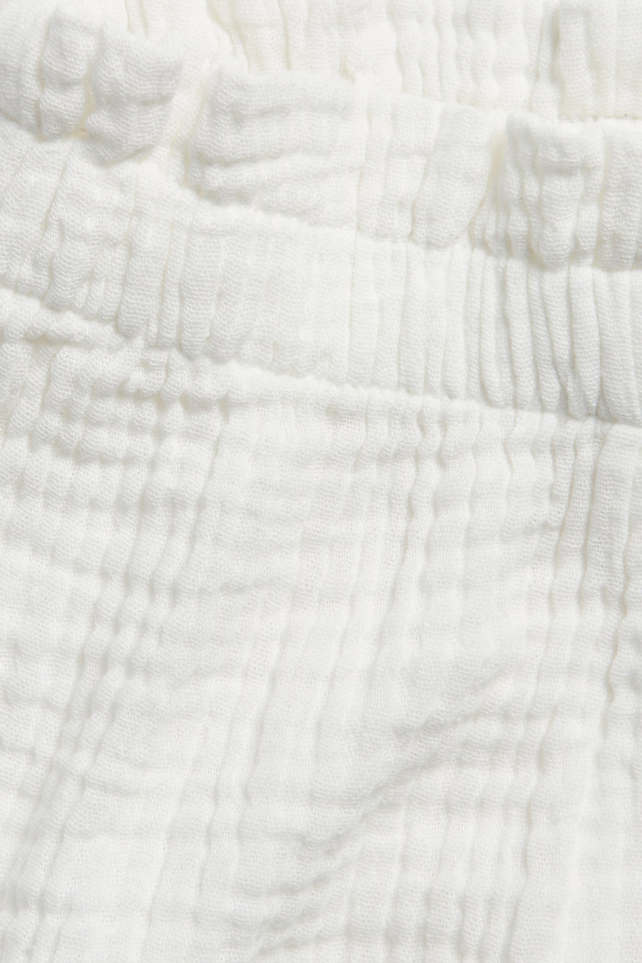 Närbild av offwhite muslinshorts för baby med mjuk resår i midjan.