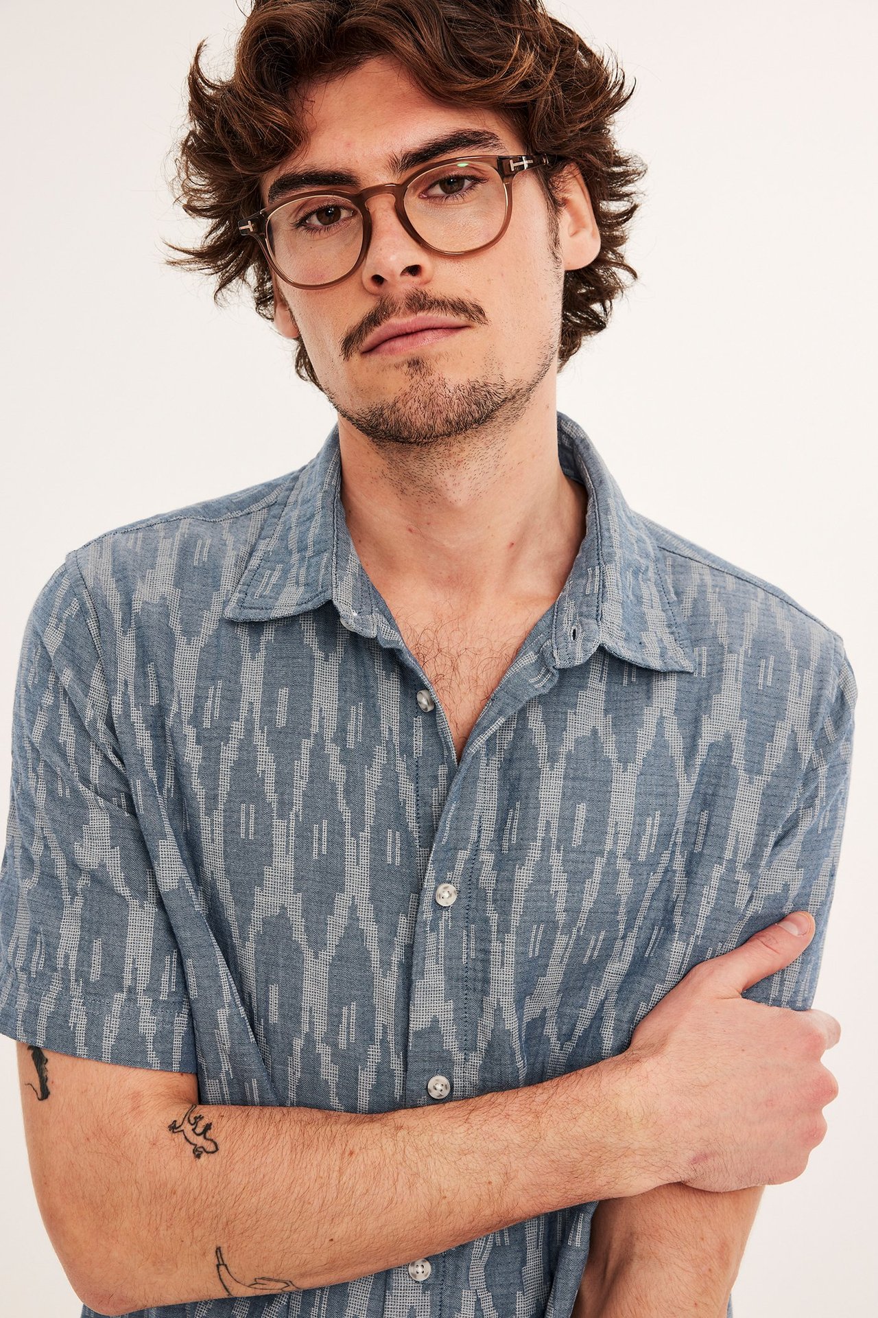 Lähikuva edestä miehestä, jolla on tummansininen kuviollinen lyhythihainen puuvillapaita ja ruskeat lasit.