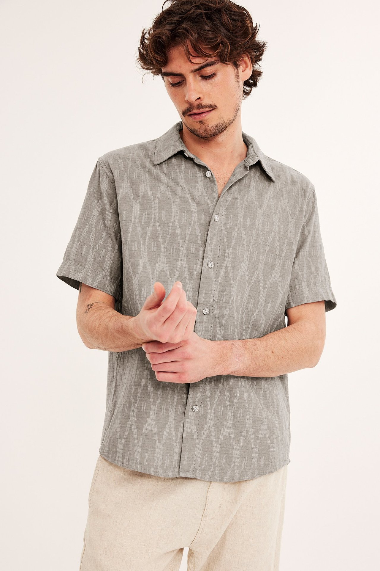 Edestä kuvattu mies harmaakuvioisessa lyhythihaisessa puuvillapaidassa ja vaaleissa beigenvärisissä housuissa.
