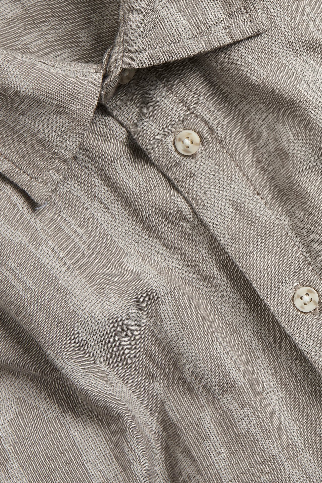 Zbliżenie jasnobrązowej, wzorzystej, bawełnianej koszuli z krótkim rękawem, z widocznymi guzikami i kołnierzem.