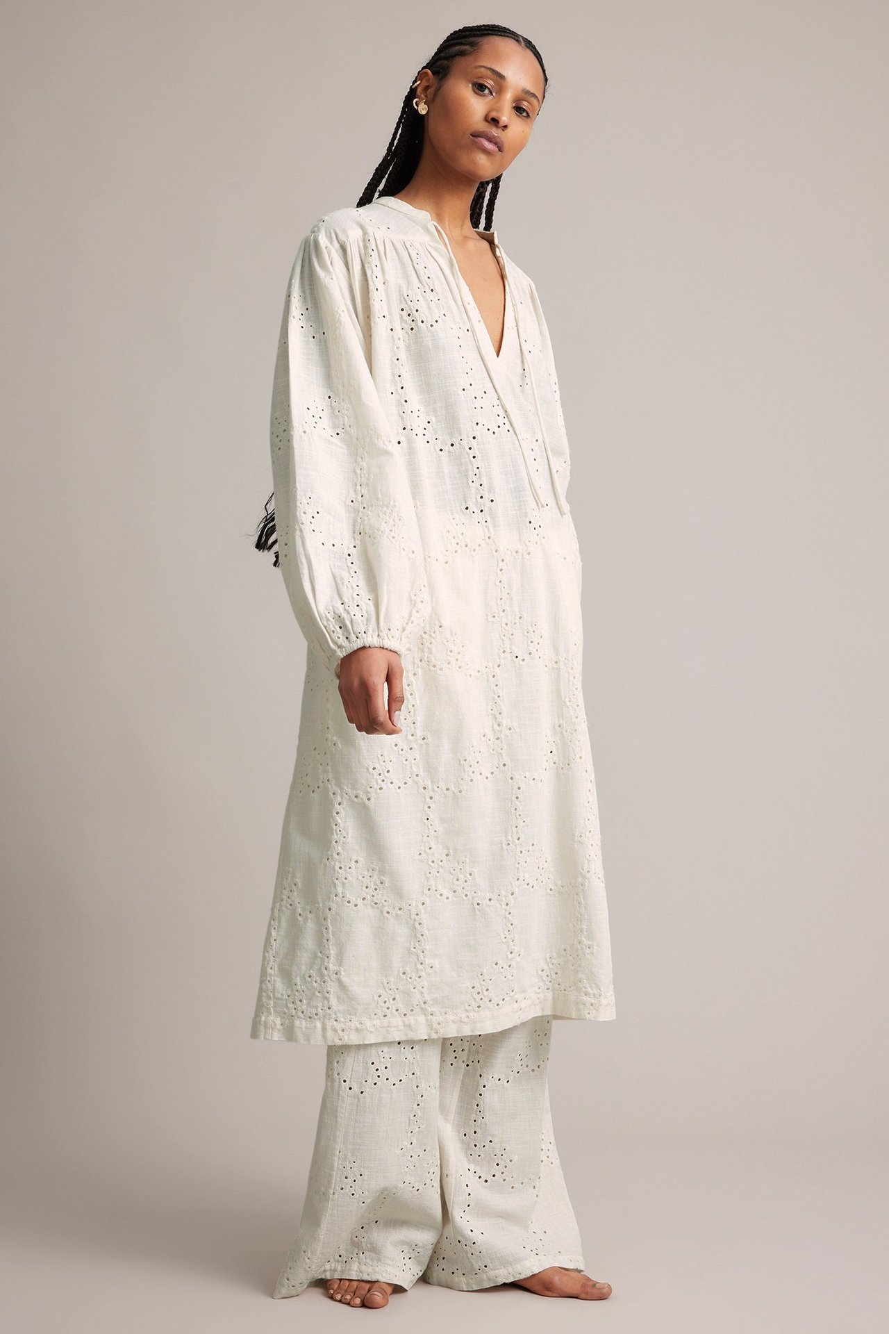 Frontbilde av en kvinne i hvit broderie anglaise midikjole med puffermer og matchende vide bukser.