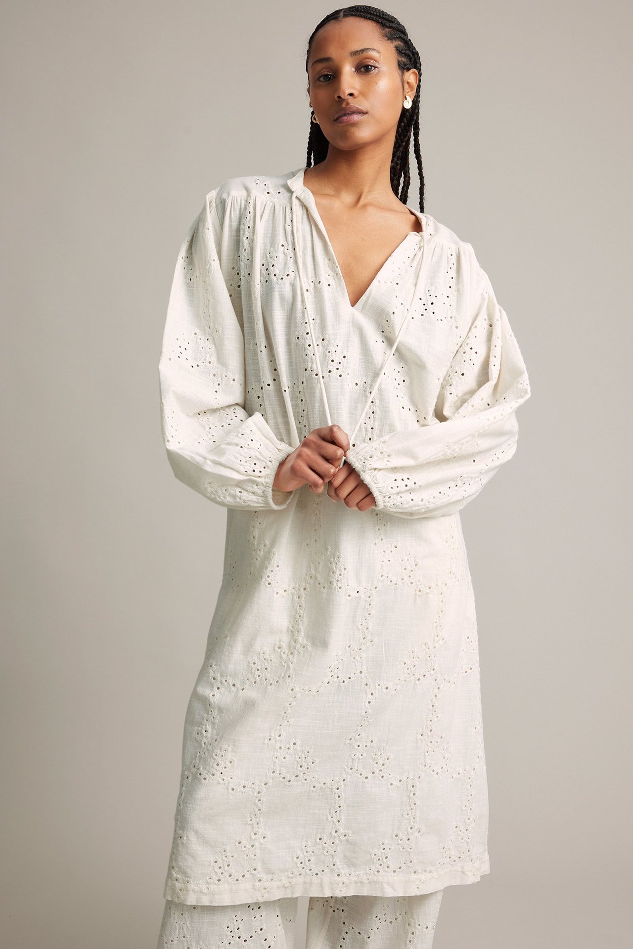 Forfra: kvinne i løs hvit brodert langermet bomullskjole med knytebånd og matchende bukser.