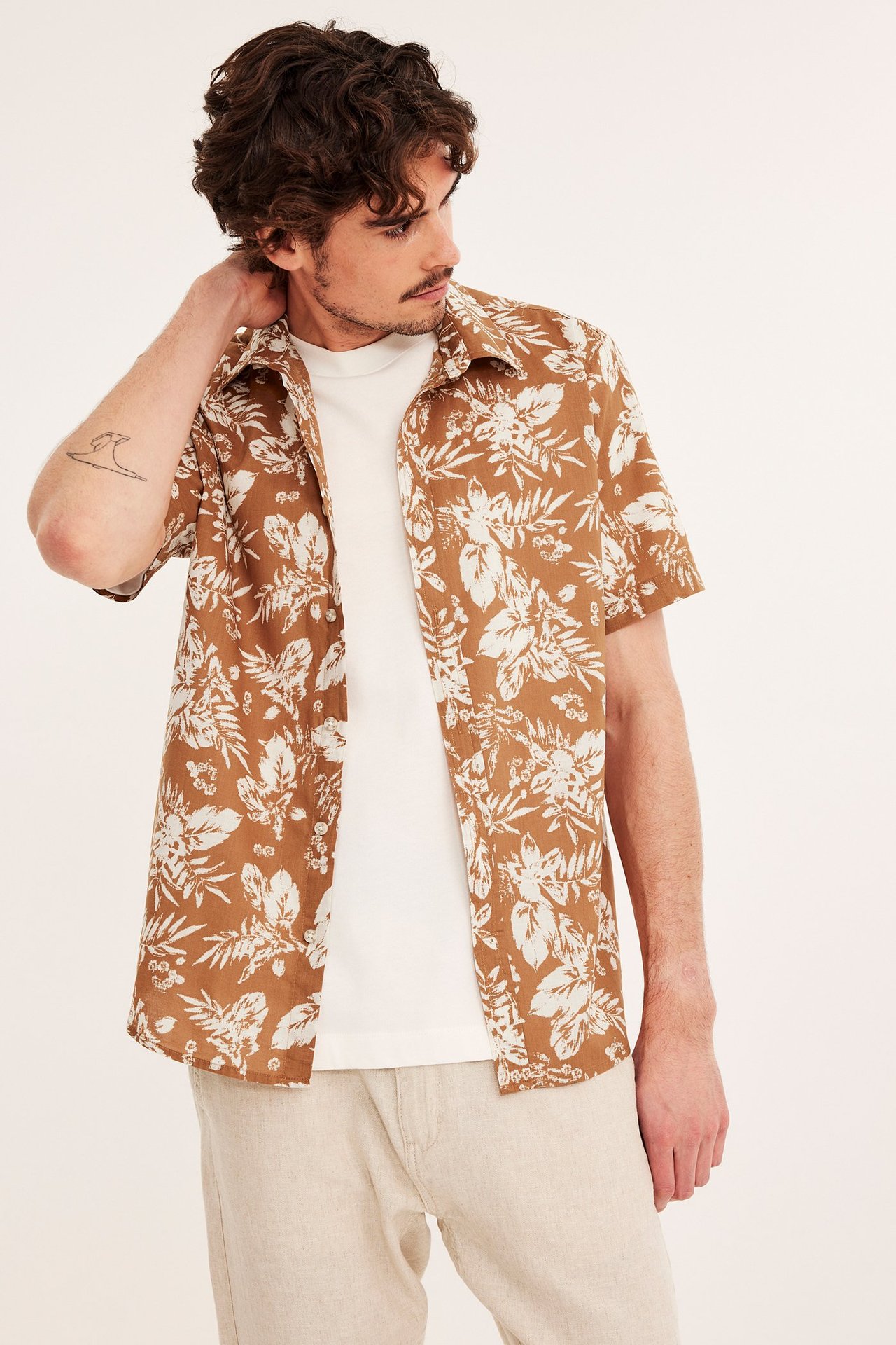 Framsida av en man i en brunmönstrad kortärmad skjorta över en vit t-shirt och beiga byxor.