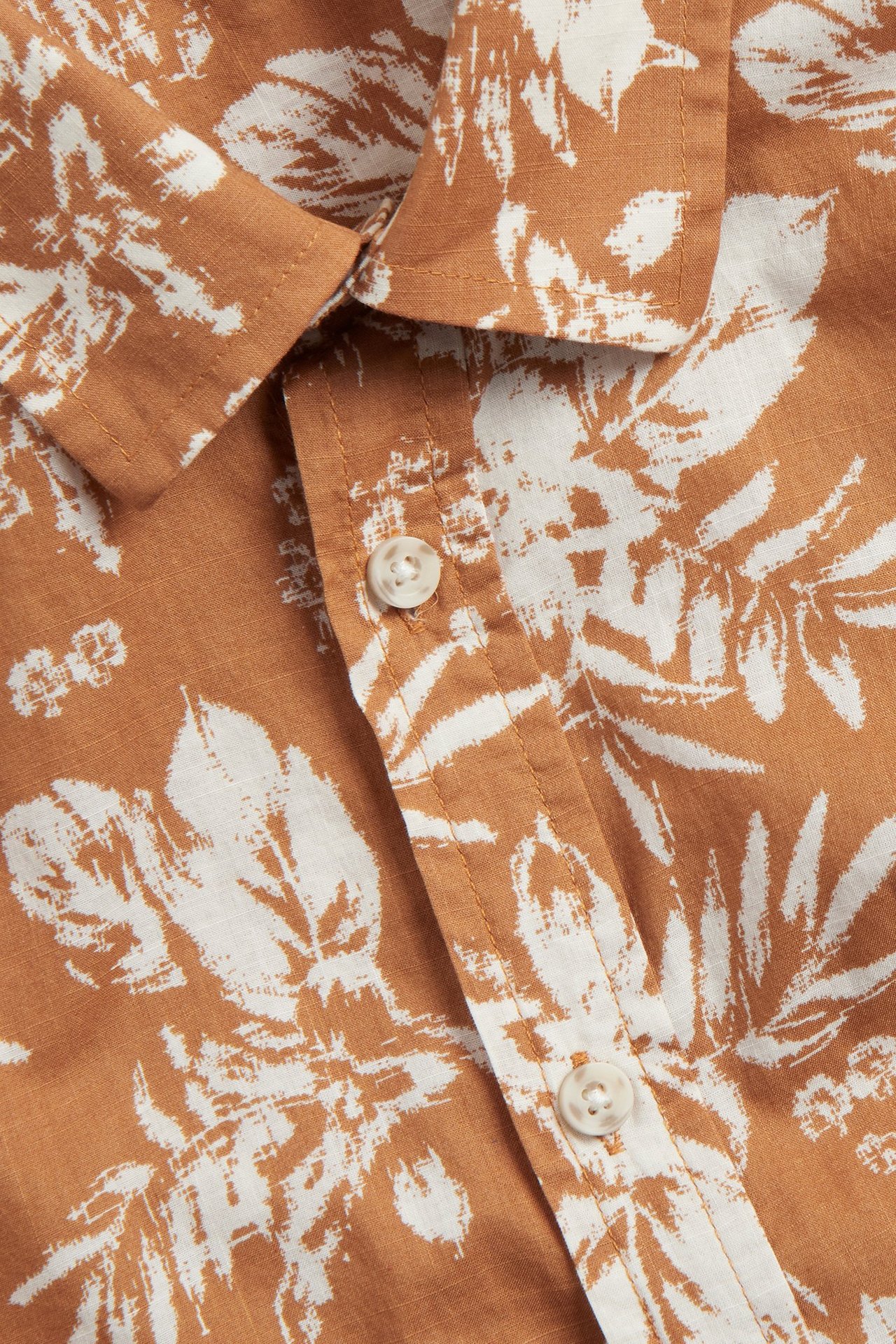 Zbliżenie brązowej bawełnianej koszuli z krótkim rękawem, z białym nadrukiem i jasnymi guzikami.