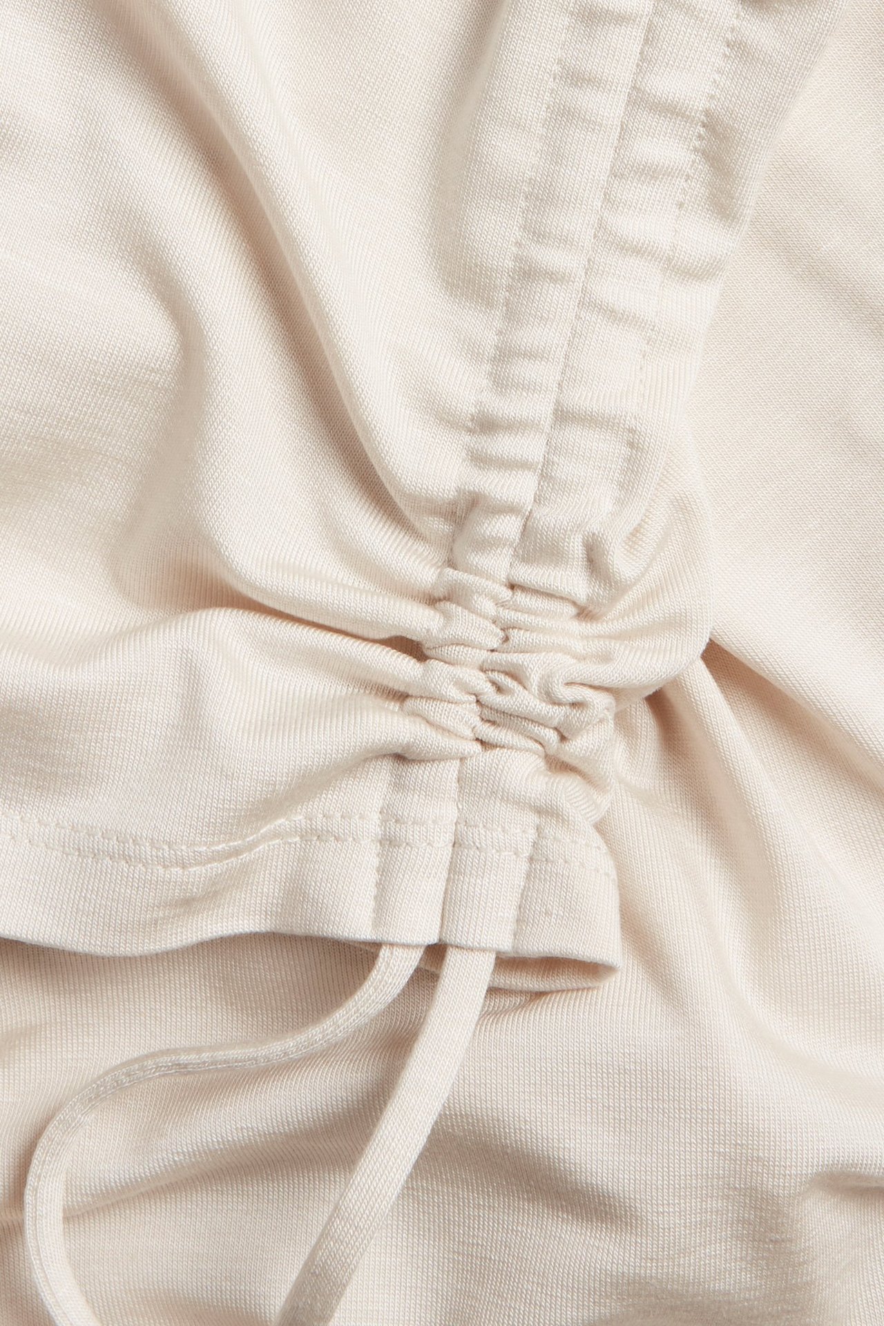 Zbliżenie na jasnobeżowy top z mieszanki tencelu z bocznym ściągaczem do regulacji marszczenia.