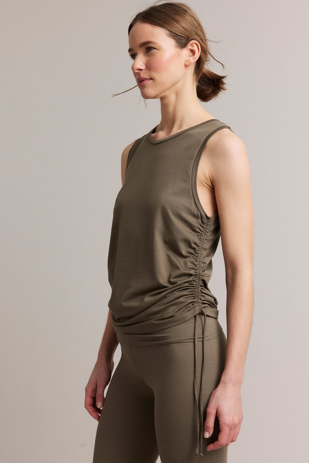 Sidevisning av en kvinne i brun tencelblandingstopp med snøring i siden og matchende brune leggings.