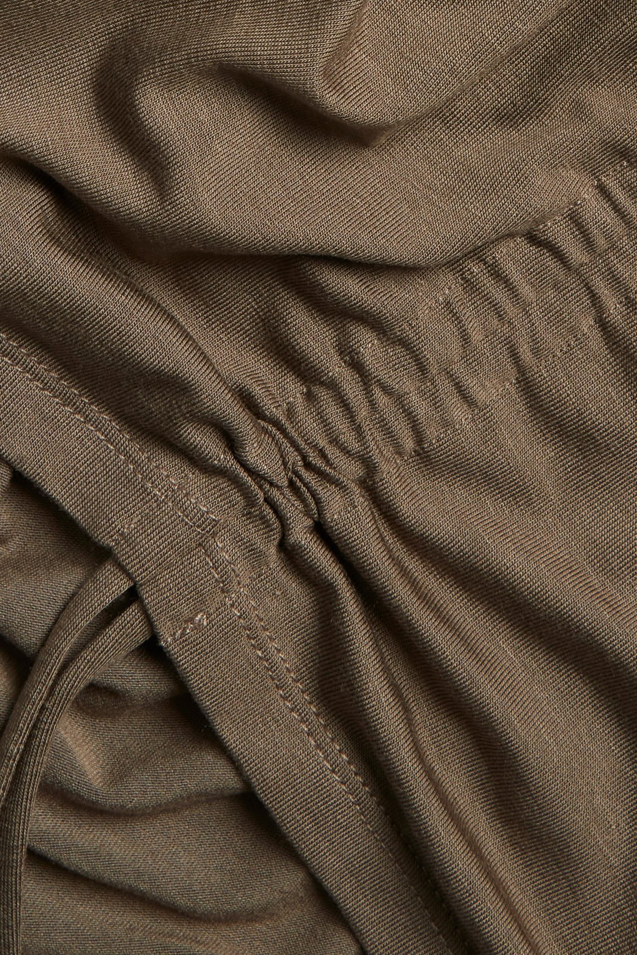 Zbliżenie brązowego topu z mieszanki tencelu z bocznymi troczkami do regulacji marszczenia.
