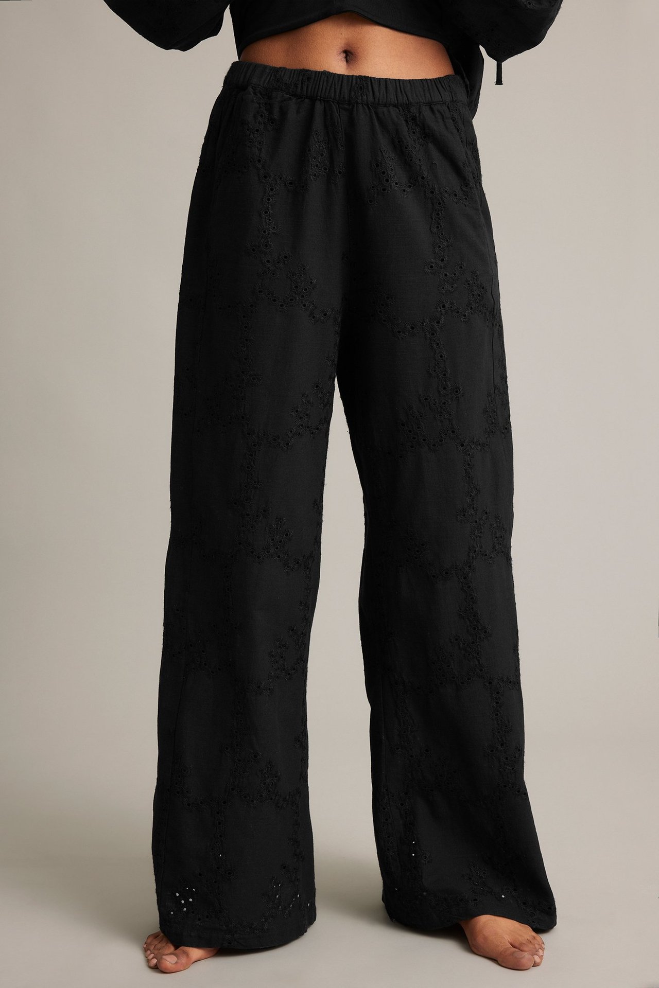 Framifrån, kvinna i svarta vida bomullsbyxor med broderie anglaise och en svart kort topp.