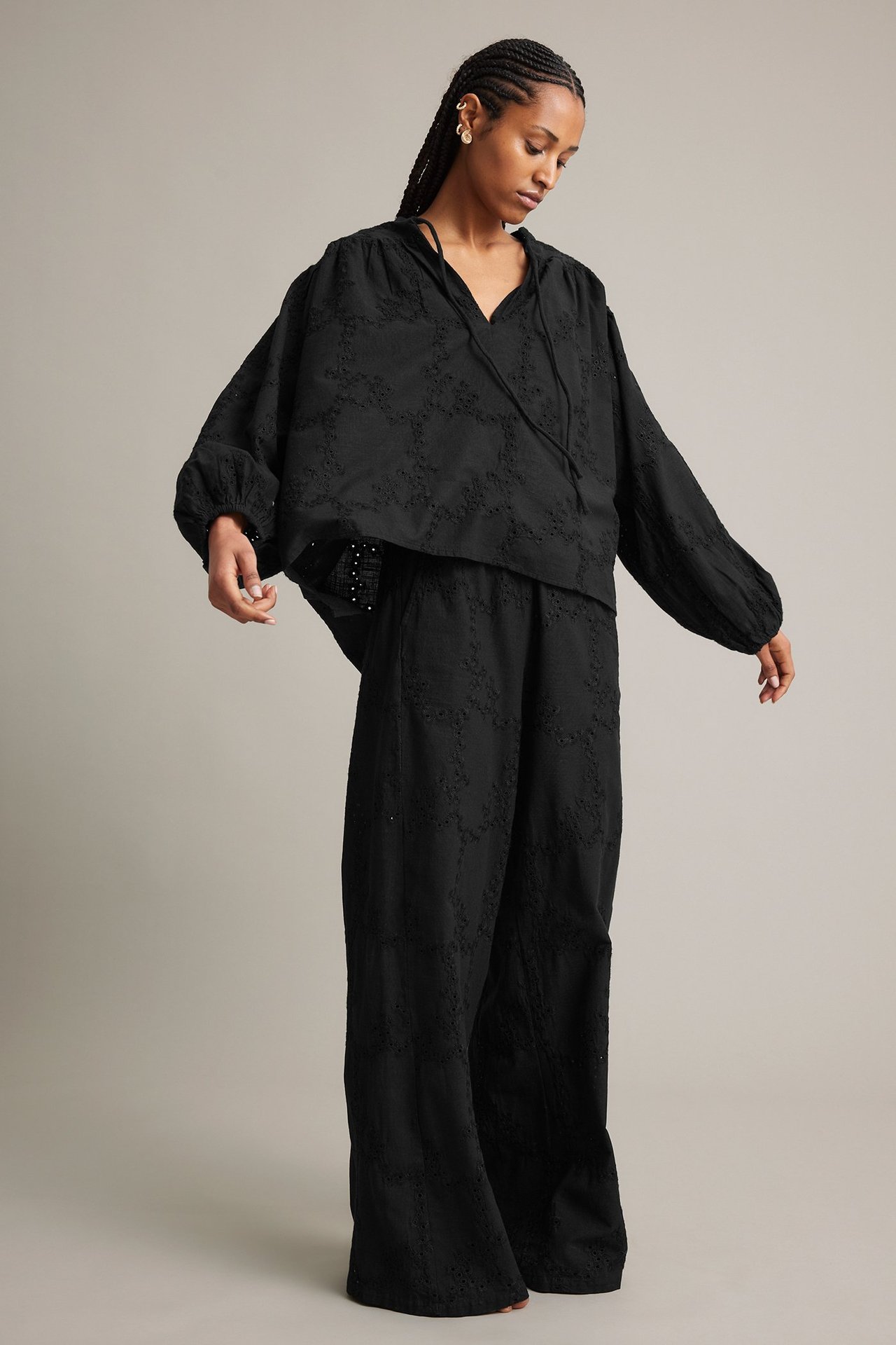 Framifrån, kvinna i svarta vida broderade bomullsbyxor och matchande svart blus.