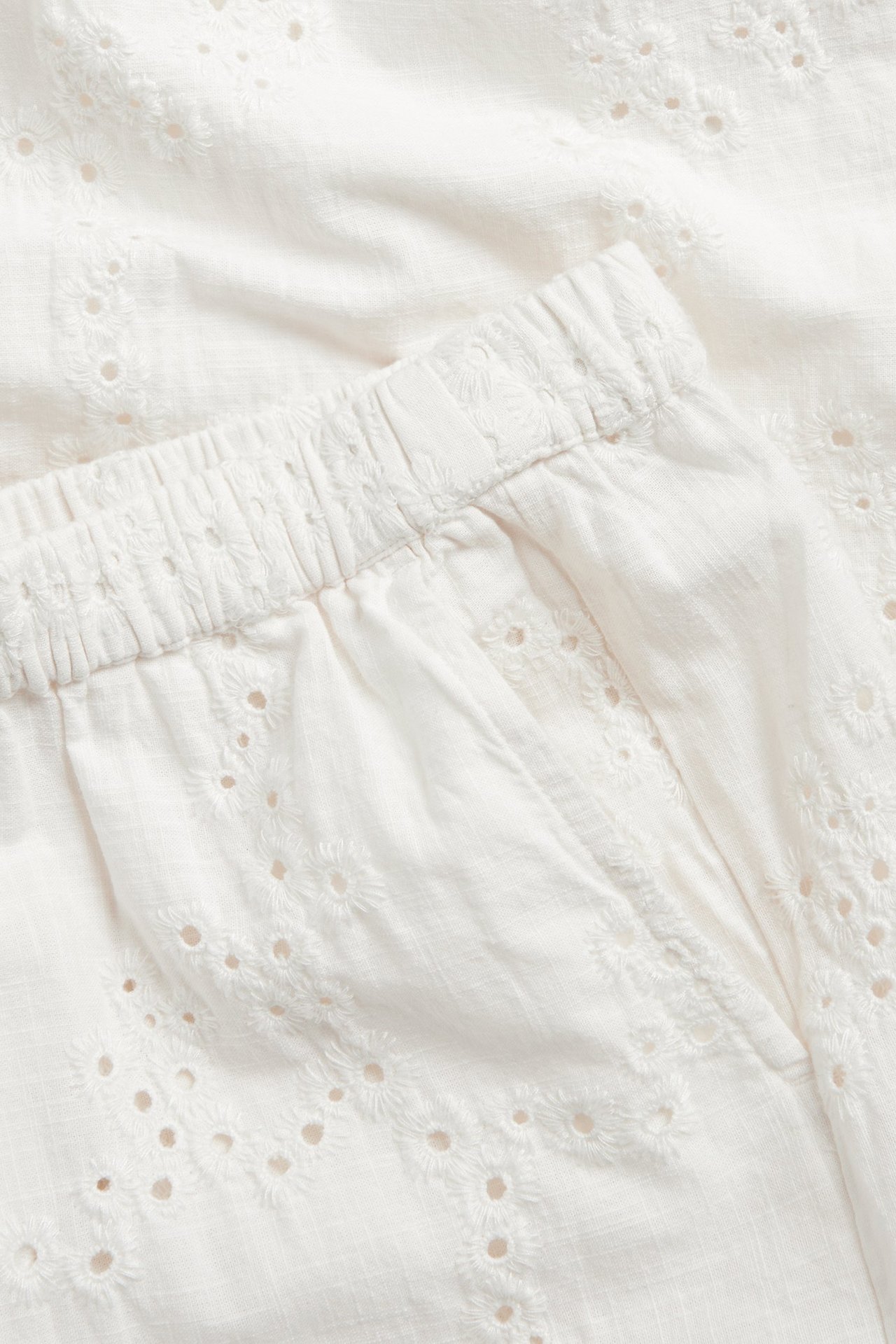 Lähikuva valkoisista leveälahkeisista puuvillahousuista, joissa on broderie anglaise, joustava vyötärö ja sivutasku.