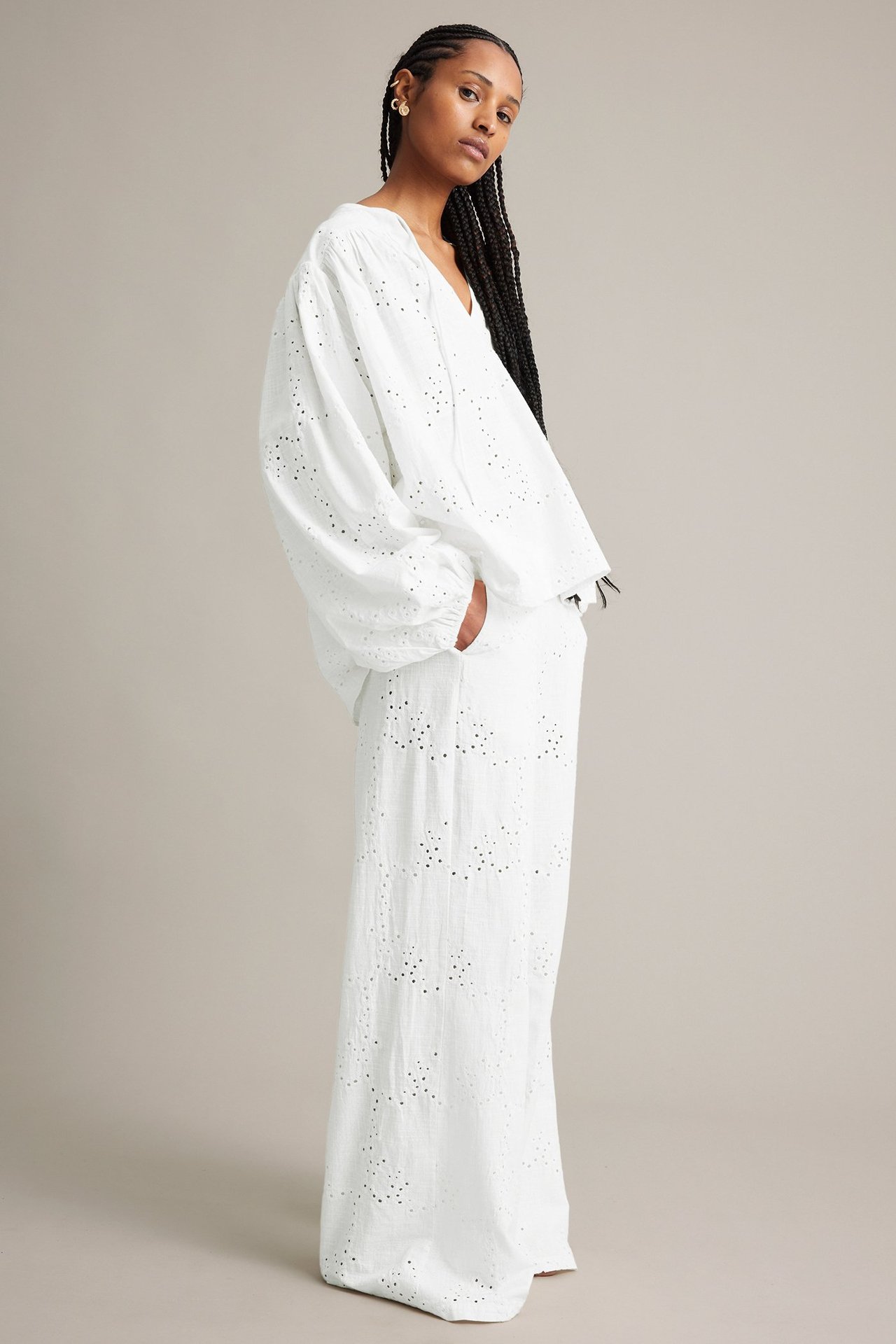 Sivukuva naisesta valkoisissa leveissä broderie anglaise -puuvillahousuissa ja yhteensopivassa löysässä puserossa.