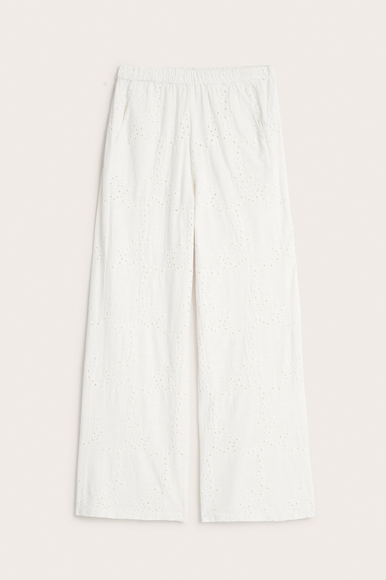 Edestä näkymä valkoisista leveälahkeisista puuvillahousuista, joissa broderie anglaise, joustovyötärö ja sivutaskut.