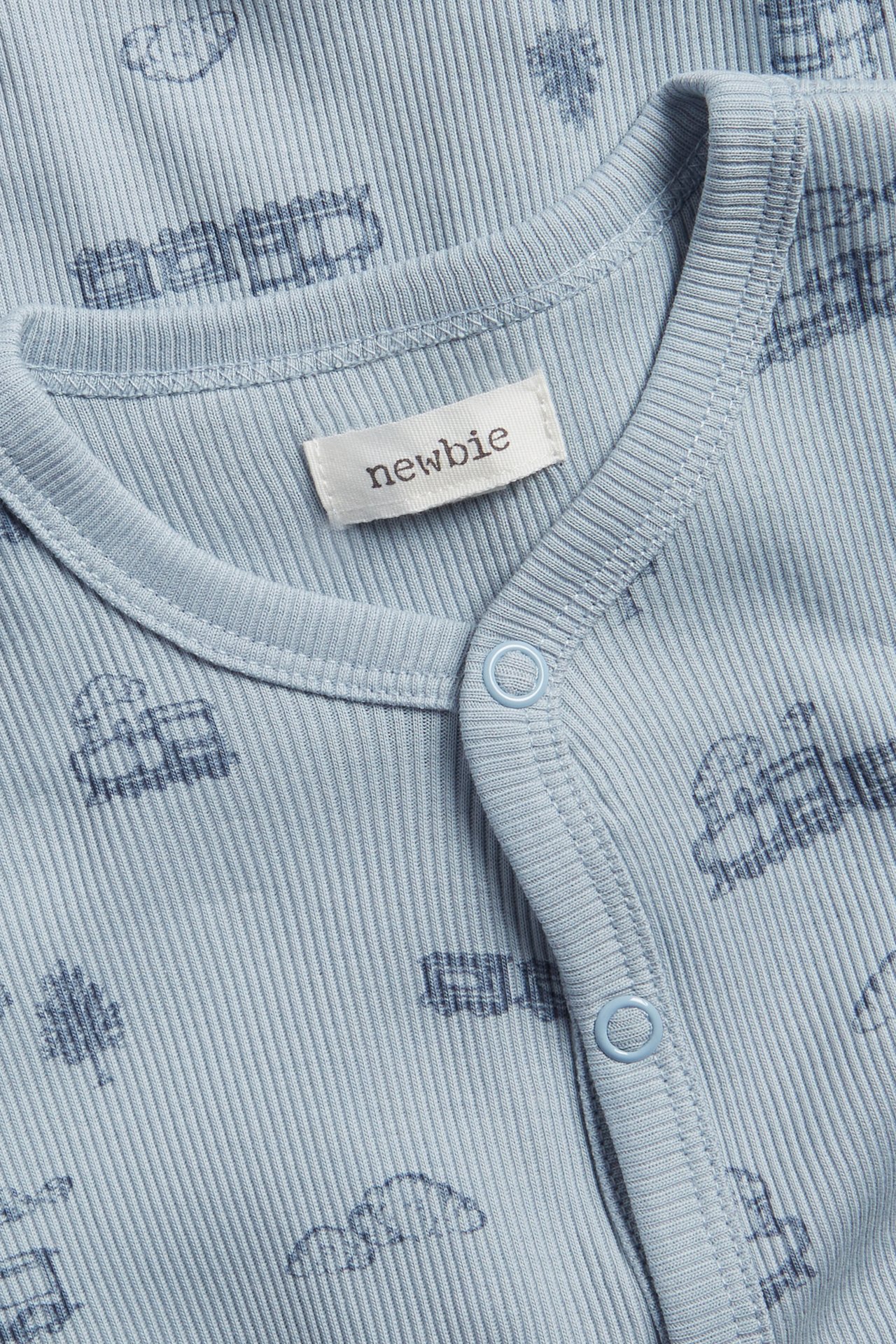 Lähikuva vaaleansinisestä ribatusta vauvan pyjamasta, jossa junakuvio ja nepparit.
