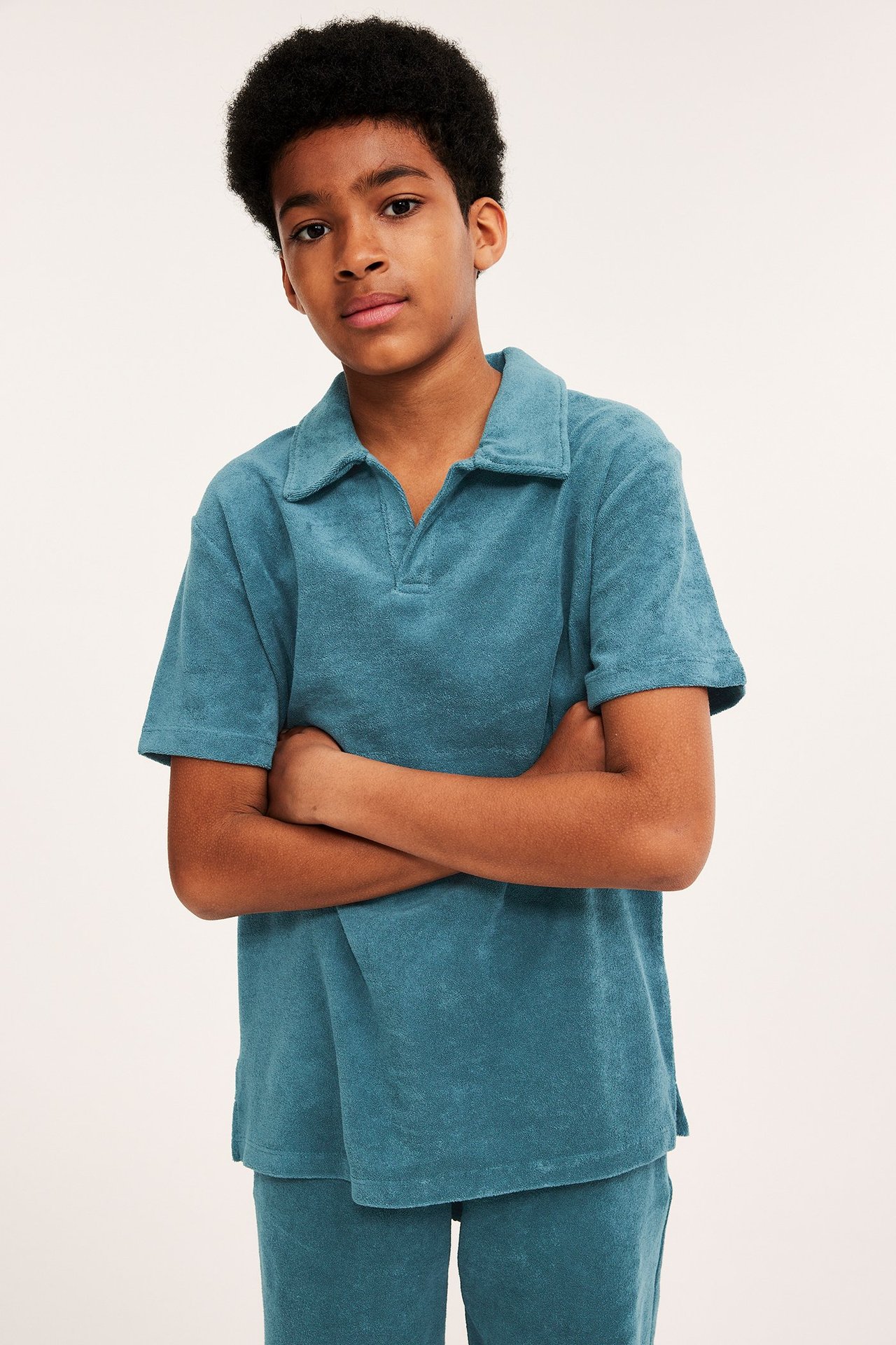 Widok z przodu dziecka w turkusowej, krótkiej koszulce polo z frotte z kołnierzykiem i pasującymi szortami.