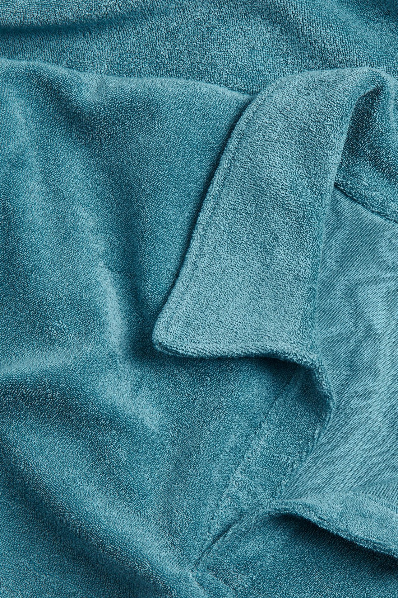 Zbliżenie na turkusową koszulkę polo z krótkim rękawem z frotte, ukazujące jej miękką fakturę.