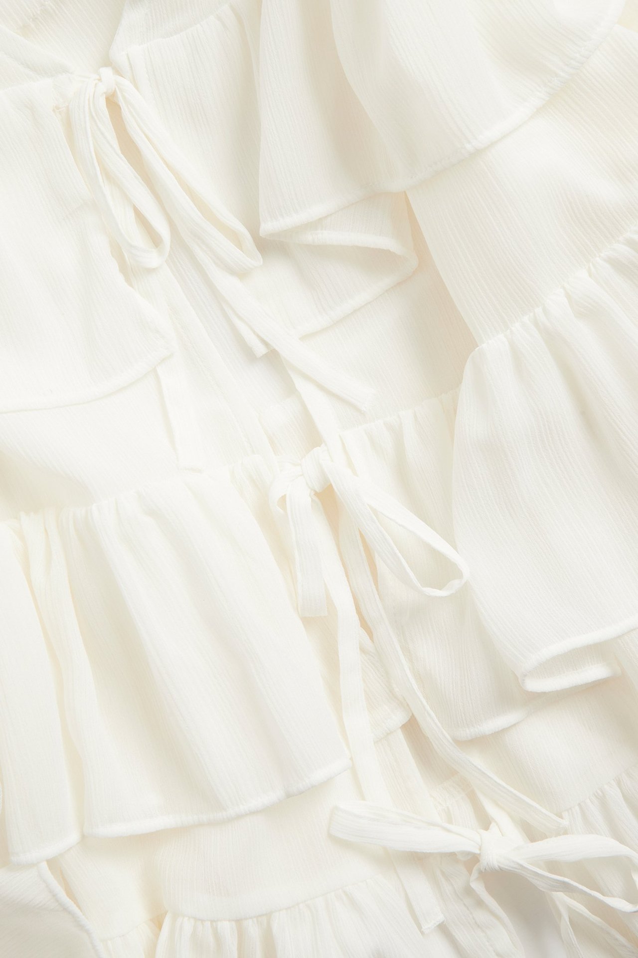 Zbliżenie na ecru bluzkę szyfonową z licznymi falbanami i wiązaniami z przodu.