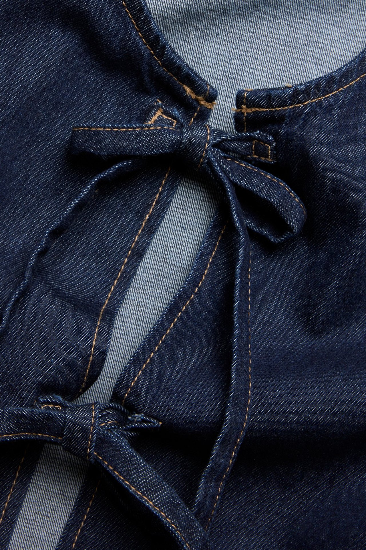 Zbliżenie ciemnej bluzki dżinsowej z wiązaniem z przodu i widocznymi kontrastowymi szwami.