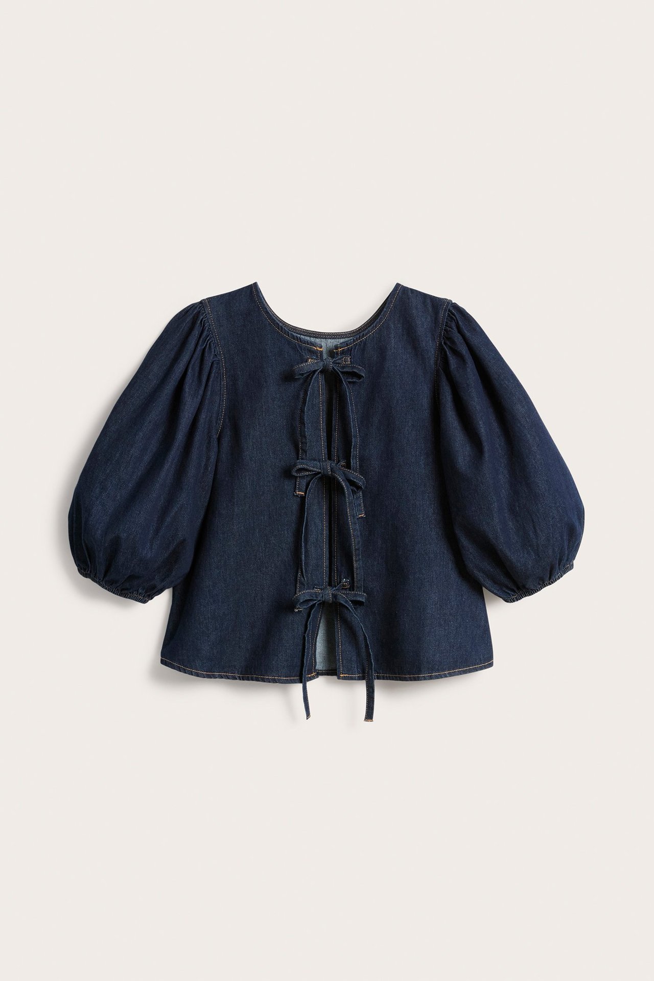 Widok z tyłu: ciemna dżinsowa bluzka damska z bufiastymi rękawami i trzema wiązaniami z tyłu.