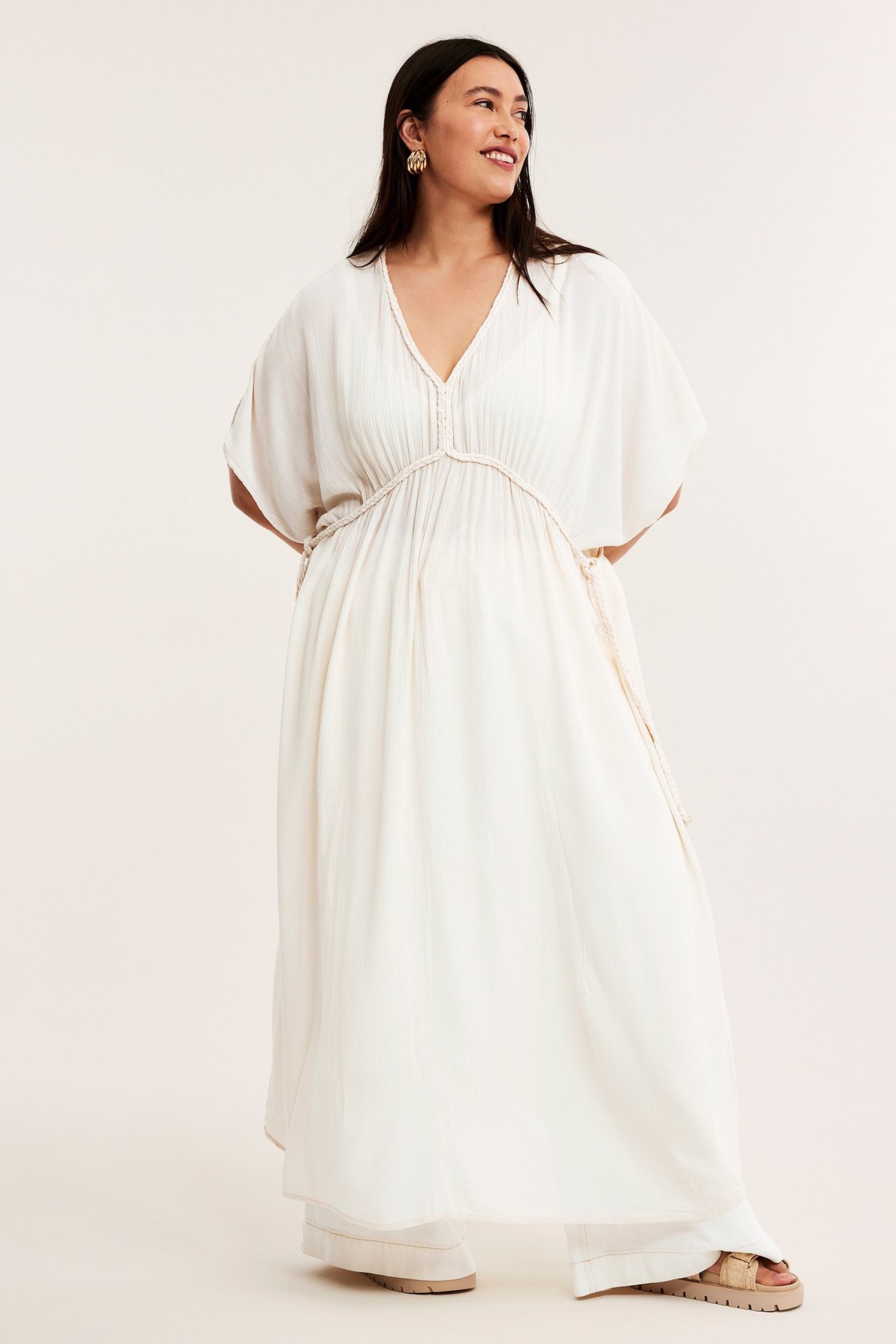 Frontalvisning: kvinne i offwhite krøllet viskose maxikjole med flettede knytebånd, gulløreringer, beige sandaler.