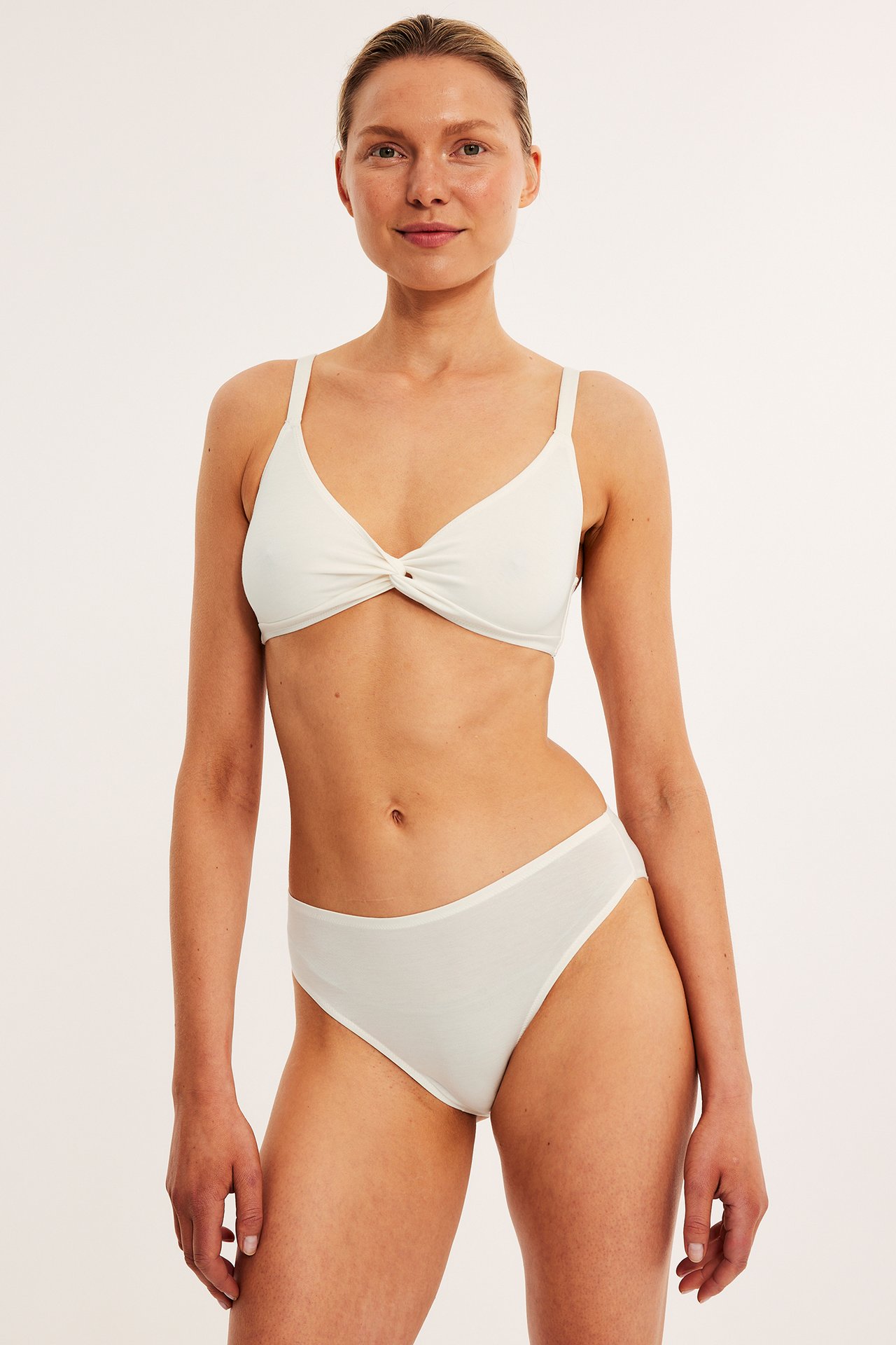 Framifrån, kvinna i vita Brazilian-trosor i mjuk Tencel och matchande vit BH med vriden front.