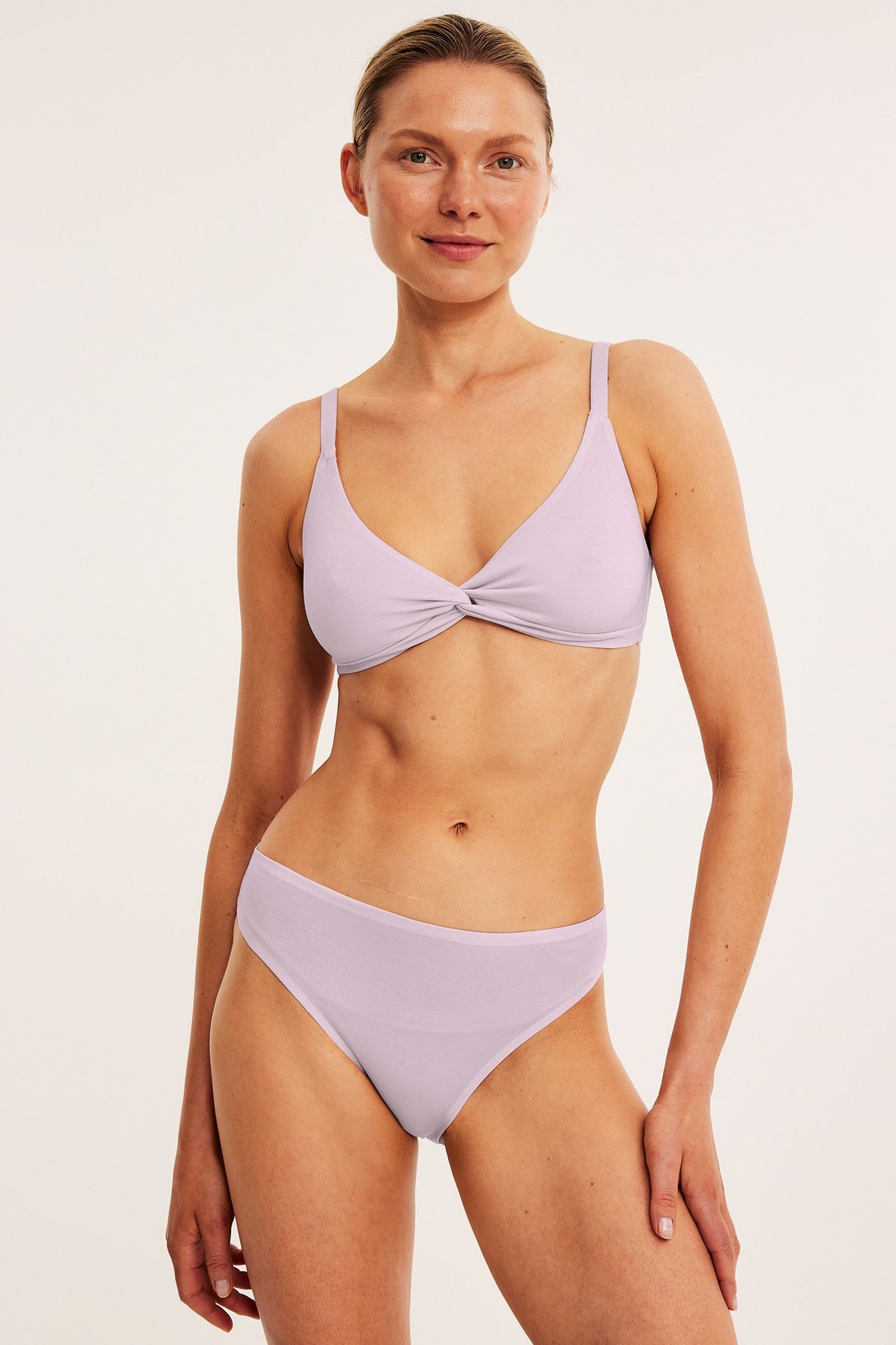 Frontbilde av en kvinne i lyserosa Tencel Brazilian truser og en matchende BH med vridd front.