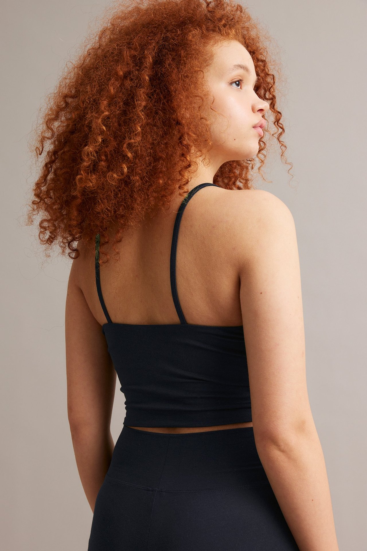 Bakfra av en kvinne i en mørkeblå, ettersittende singlet med tynne stropper og matchende leggings.