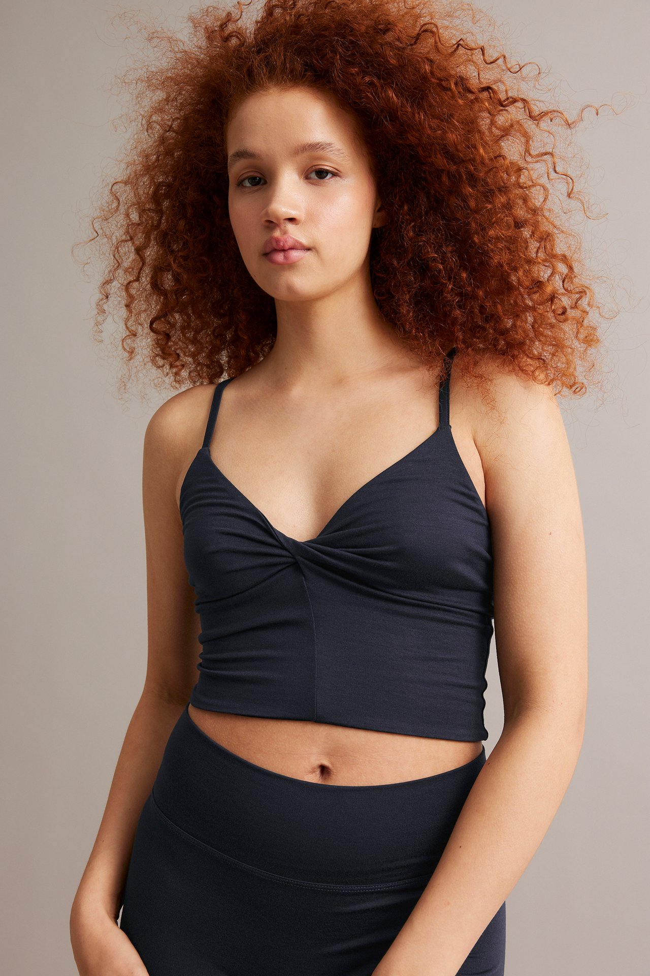 Kobieta w granatowym krótkim topie z dekoltem V ze skręceniem, cienkie ramiączka, pasujący dół.