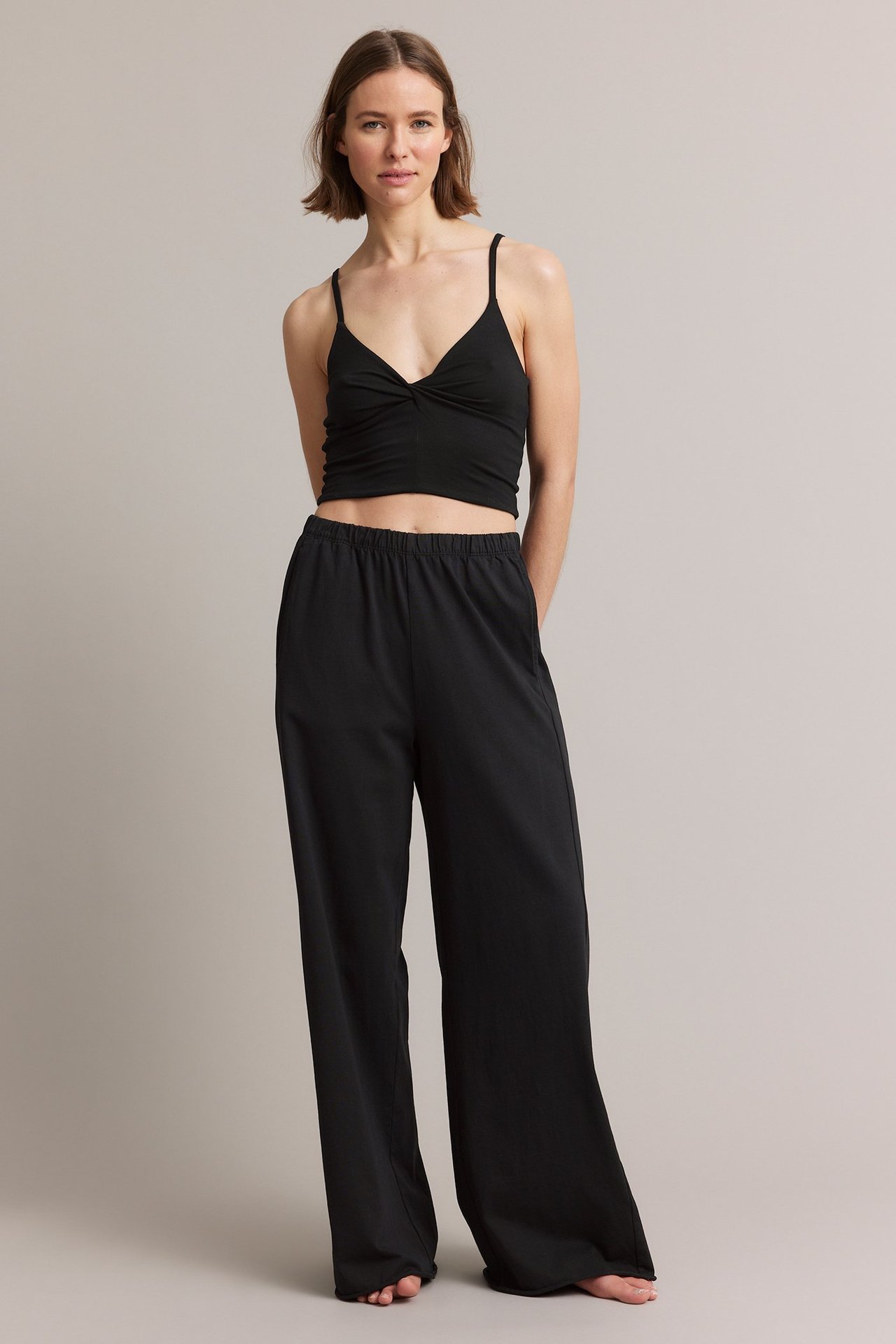Frontvisning av kvinne i svart viskoseblandet loungetopp med vridd detalj og svarte vide bukser.
