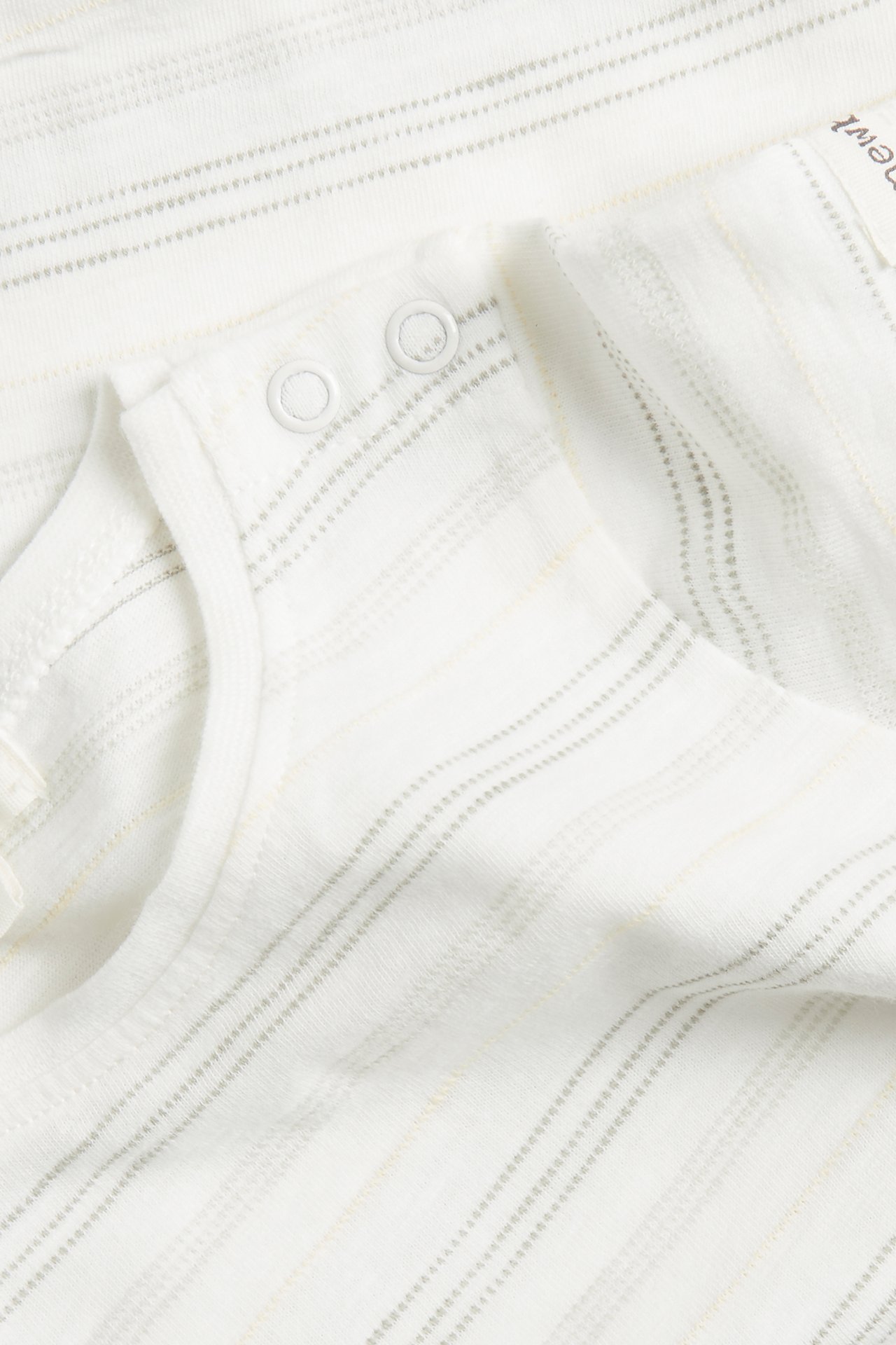 Närbild av en offwhite randig kortärmad babybody i bomull med tryckknappar på axeln.