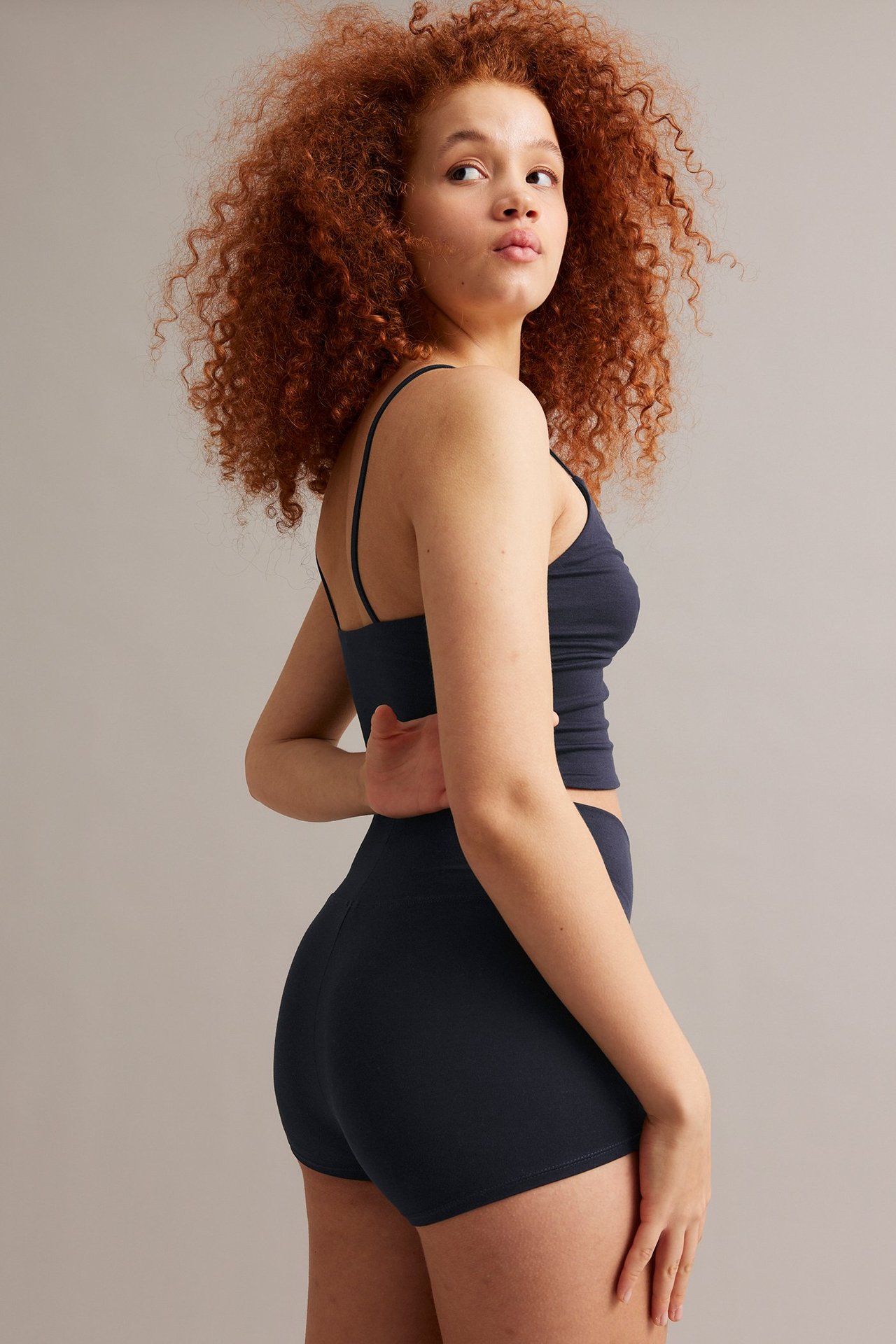 Naisen sivukuva tummansinisissä yksivärisissä bokserishortseissa ja yhteensopivassa spagettiolkaimellisessa topissa.