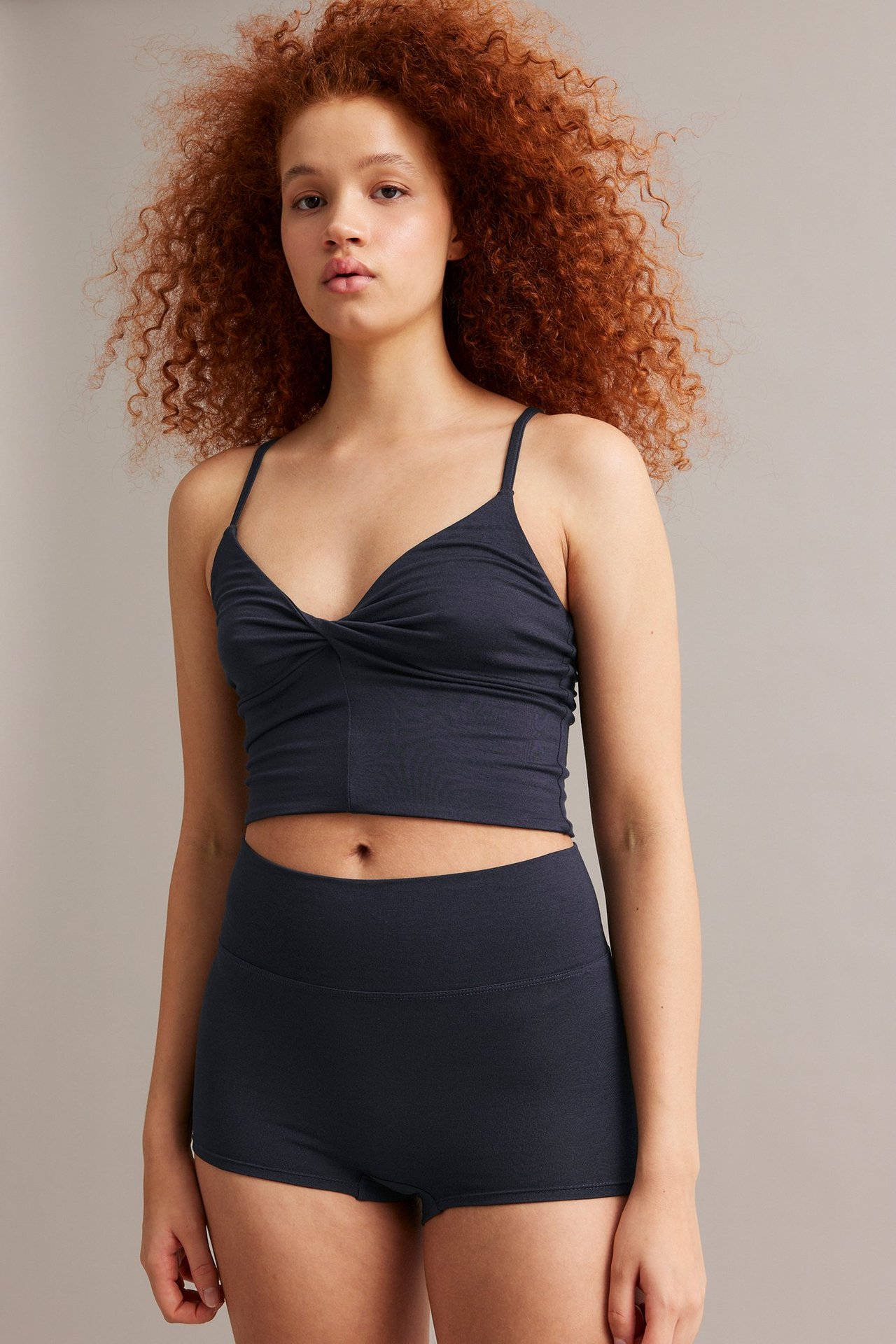 Widok z przodu kobiety w ciemnoniebieskich bokserskich figach z wiskozy i pasującym skręconym topie.