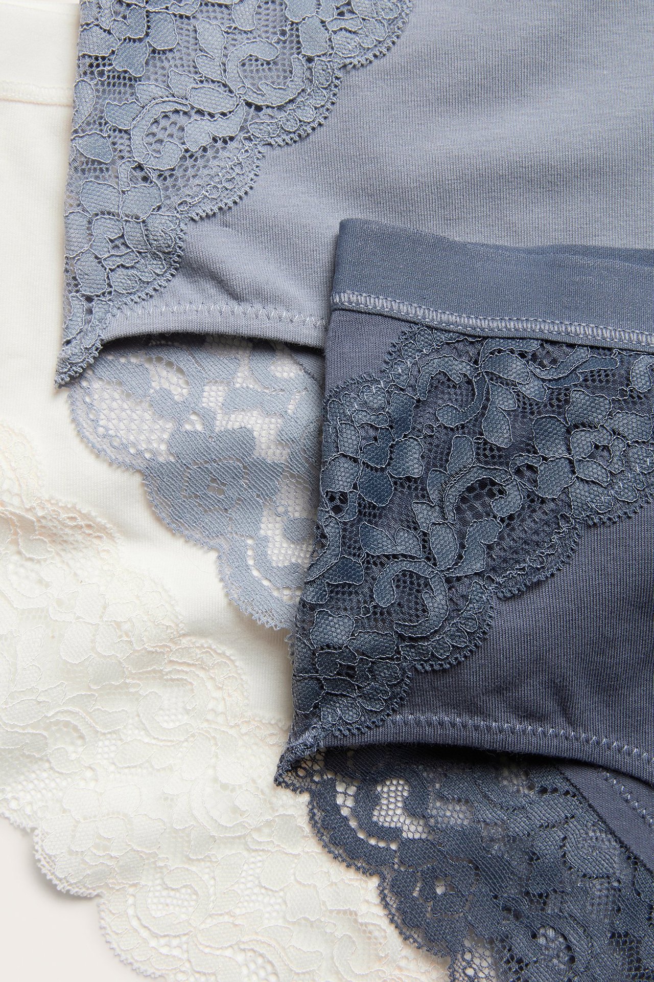 Zbliżenie trzech damskich majtek typu brief: białych, jasnoniebieskich i ciemnoniebieskich, z koronkowymi wykończeniami.