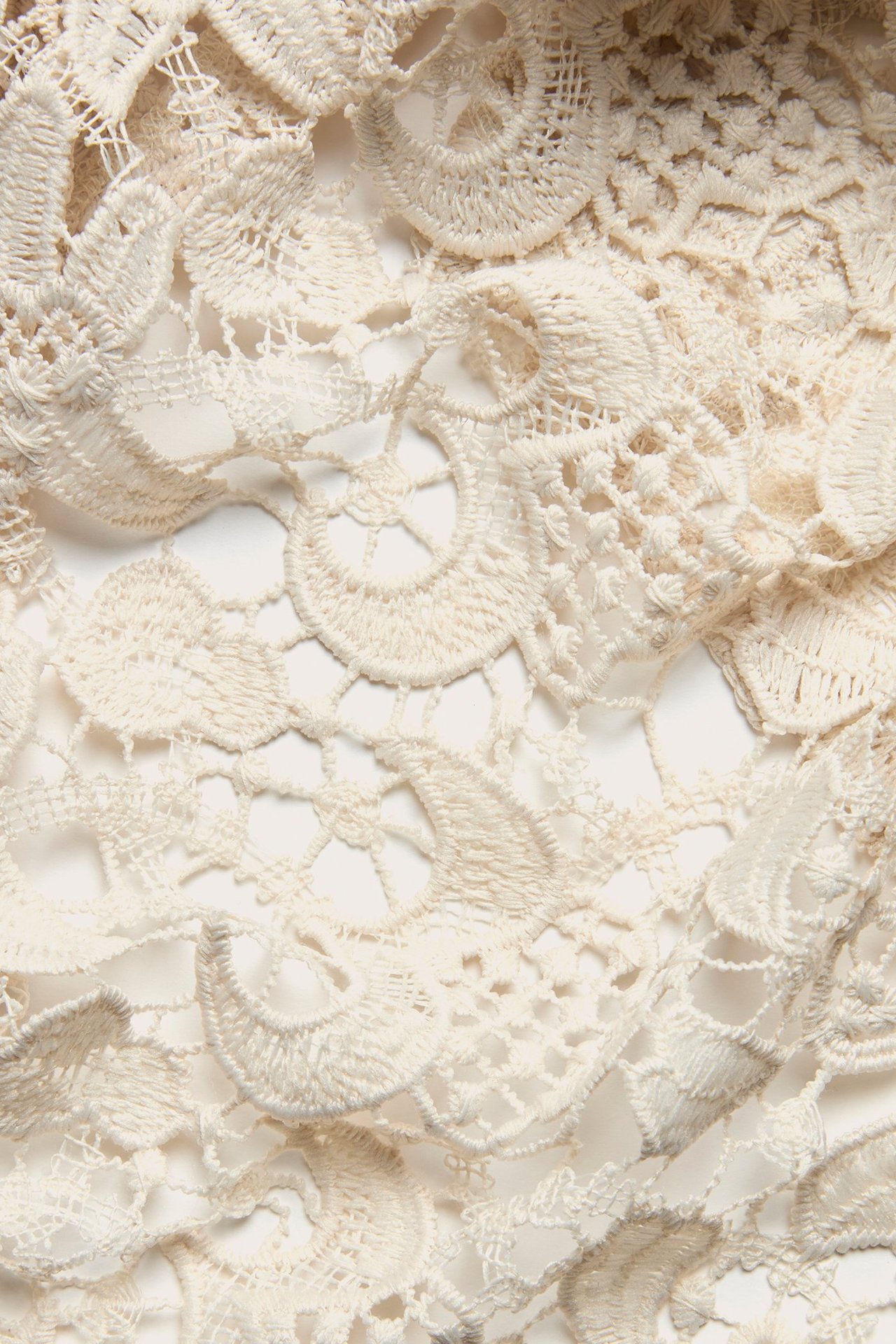 Zbliżenie na ecru koronkową tkaninę z misternymi kwiatowymi wzorami, wykonaną z poliestru.