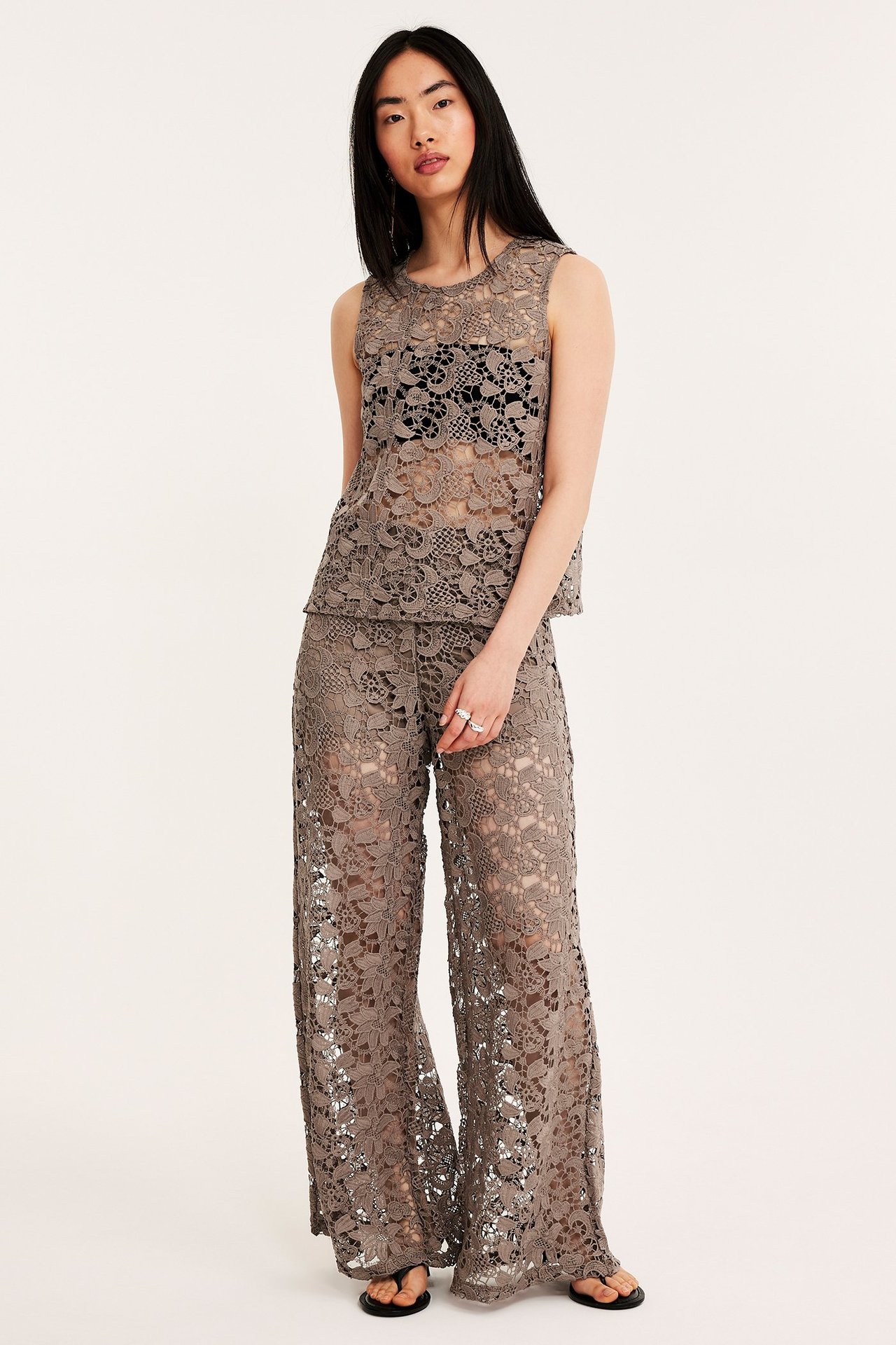 Kvinne i mørk beige blonde singlet over svart BH, matchende blondebukser og svarte flip-flops.