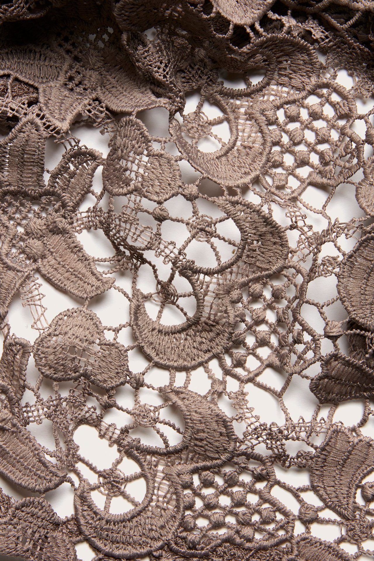 Zbliżenie na ciemnobeżowy koronkowy materiał topu z misternymi kwiatowymi wzorami.