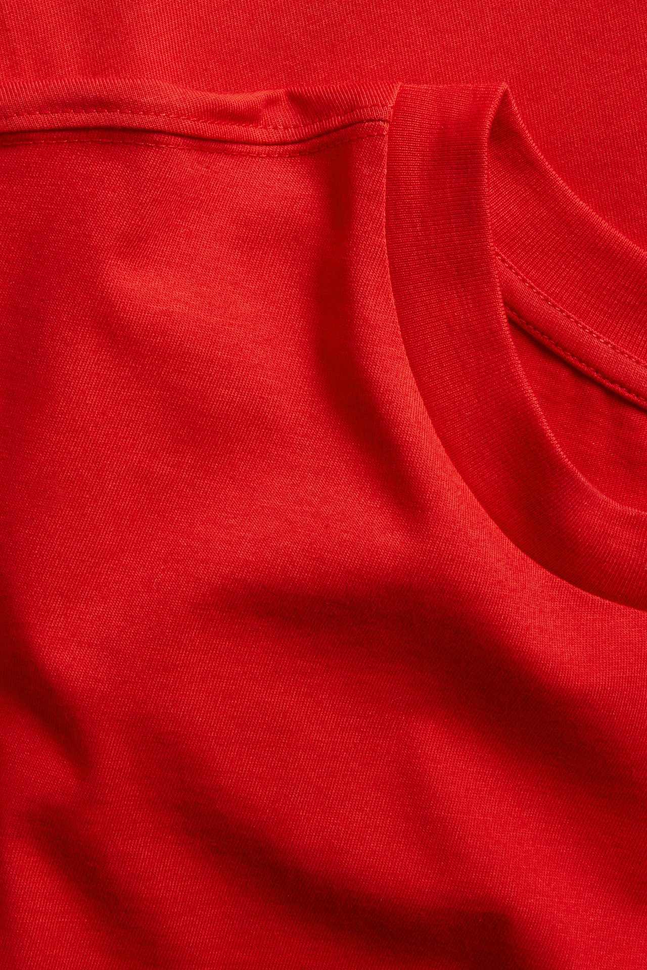 Närbild av en röd oversized boxig T-shirt i bomull, som visar tygets textur och ribbade halsringning.